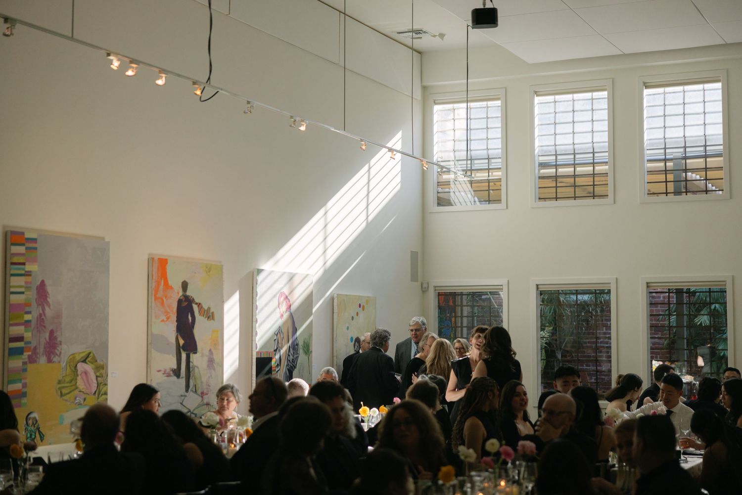 Modern reception venue with high ceilings and string lights hosting wedding guests at dining tables.