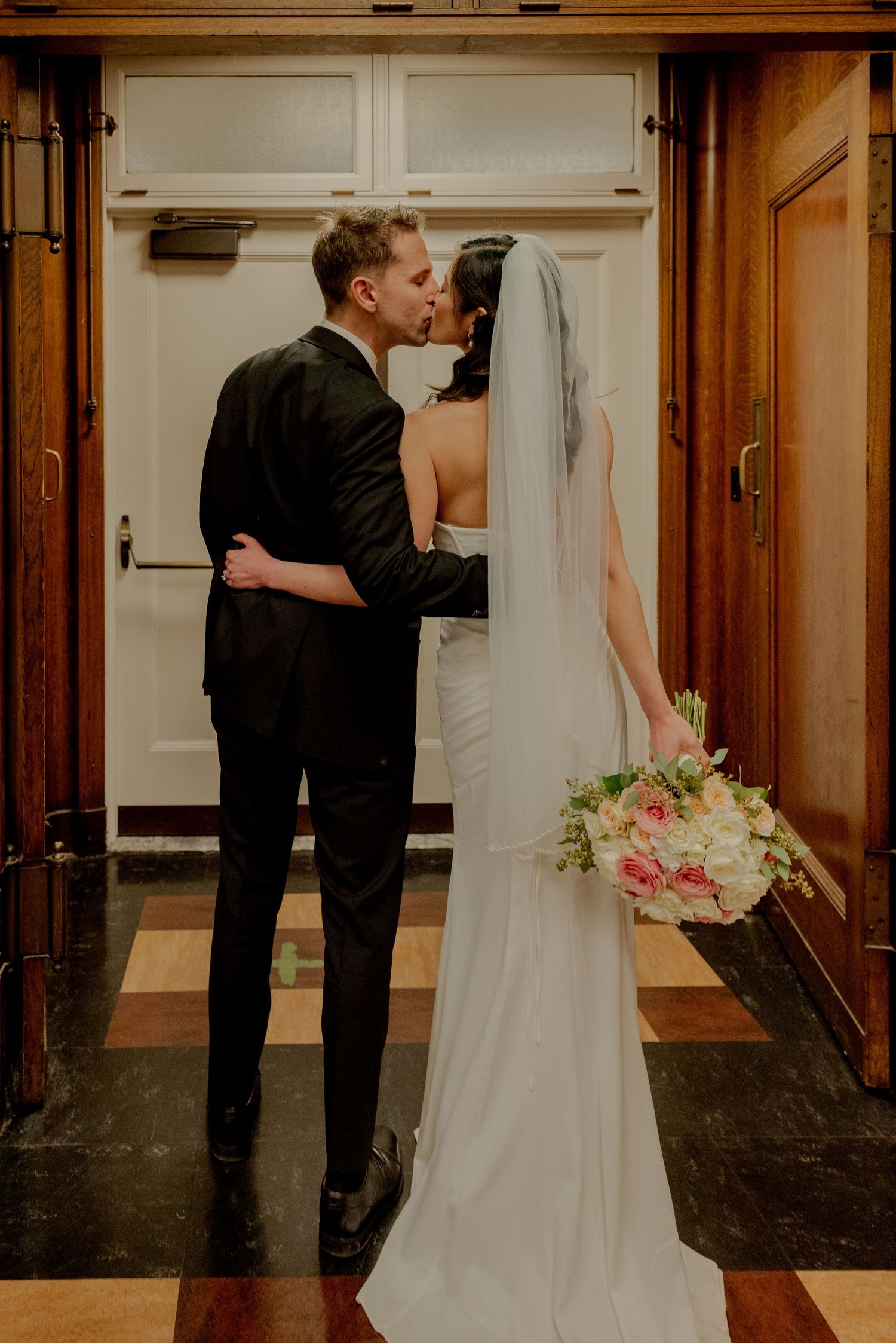 Seattle, A wedding couple shares a tender moment in a dimly lit hallway, with the bride wearing a white gown and pink floral accents.