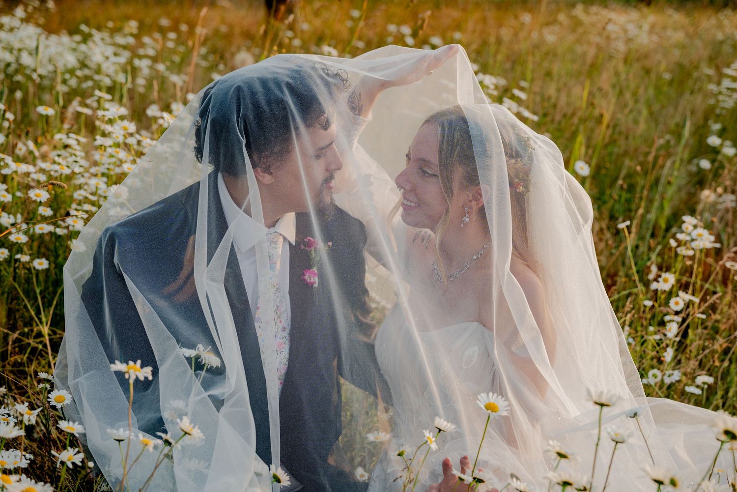 Puyallup, Washington, A romantic wedding couple shares an intimate moment under a veil in a wildflower meadow at sunset.