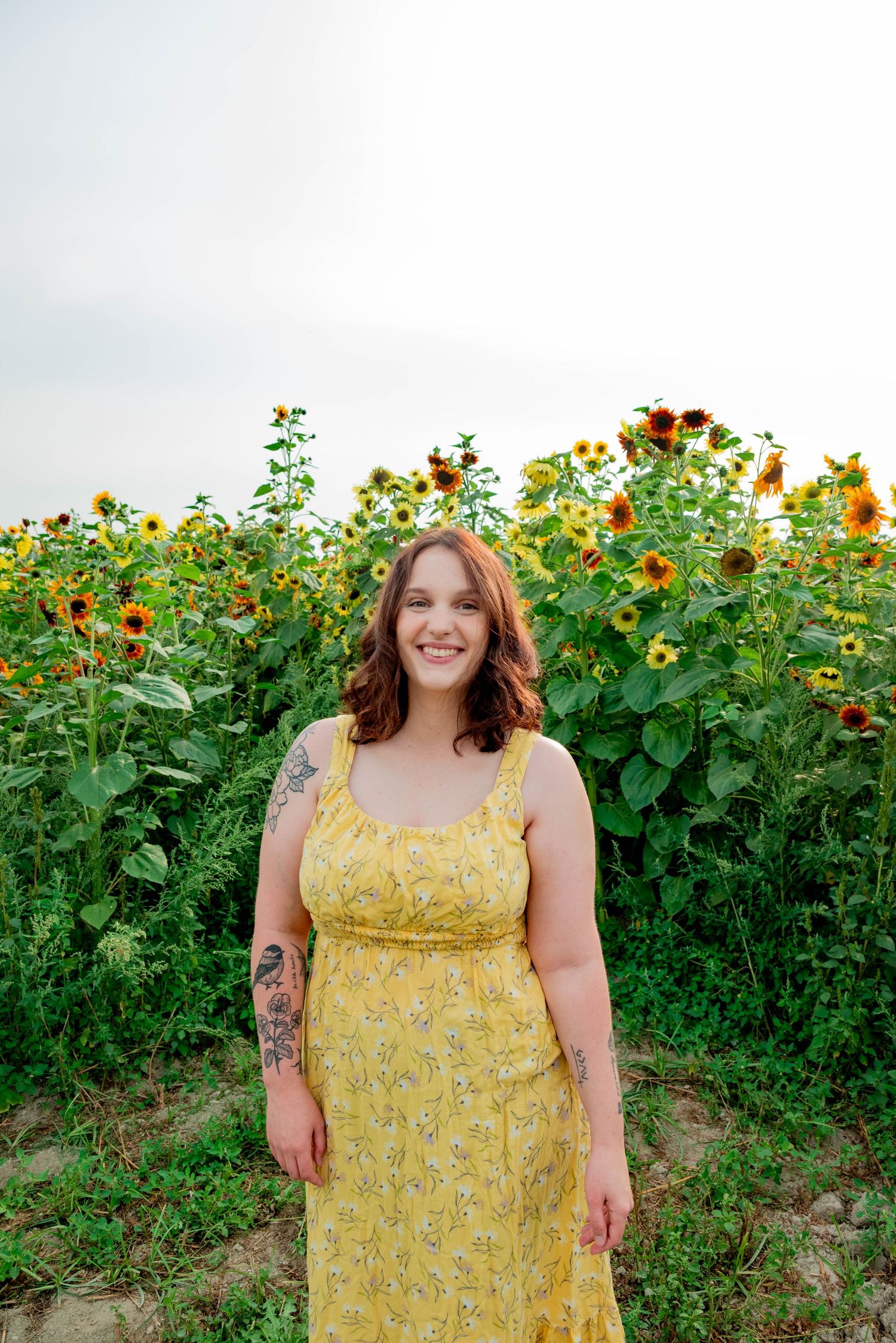 A yellow floral sundress stands out against a backdrop of tall sunflowers and greenery on a summer day.