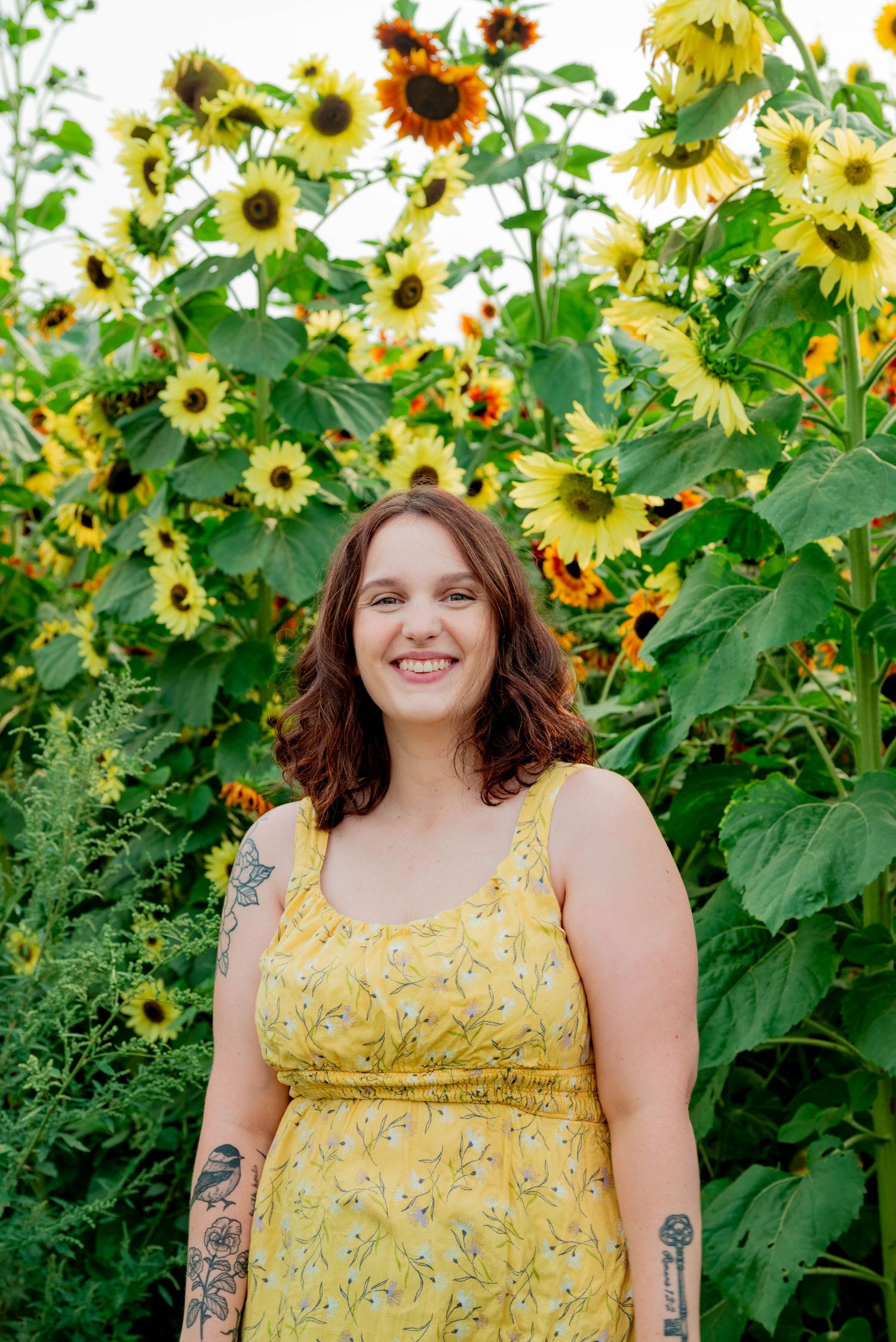 A yellow sunflower field provides a cheerful backdrop for a summer portrait in a floral dress.