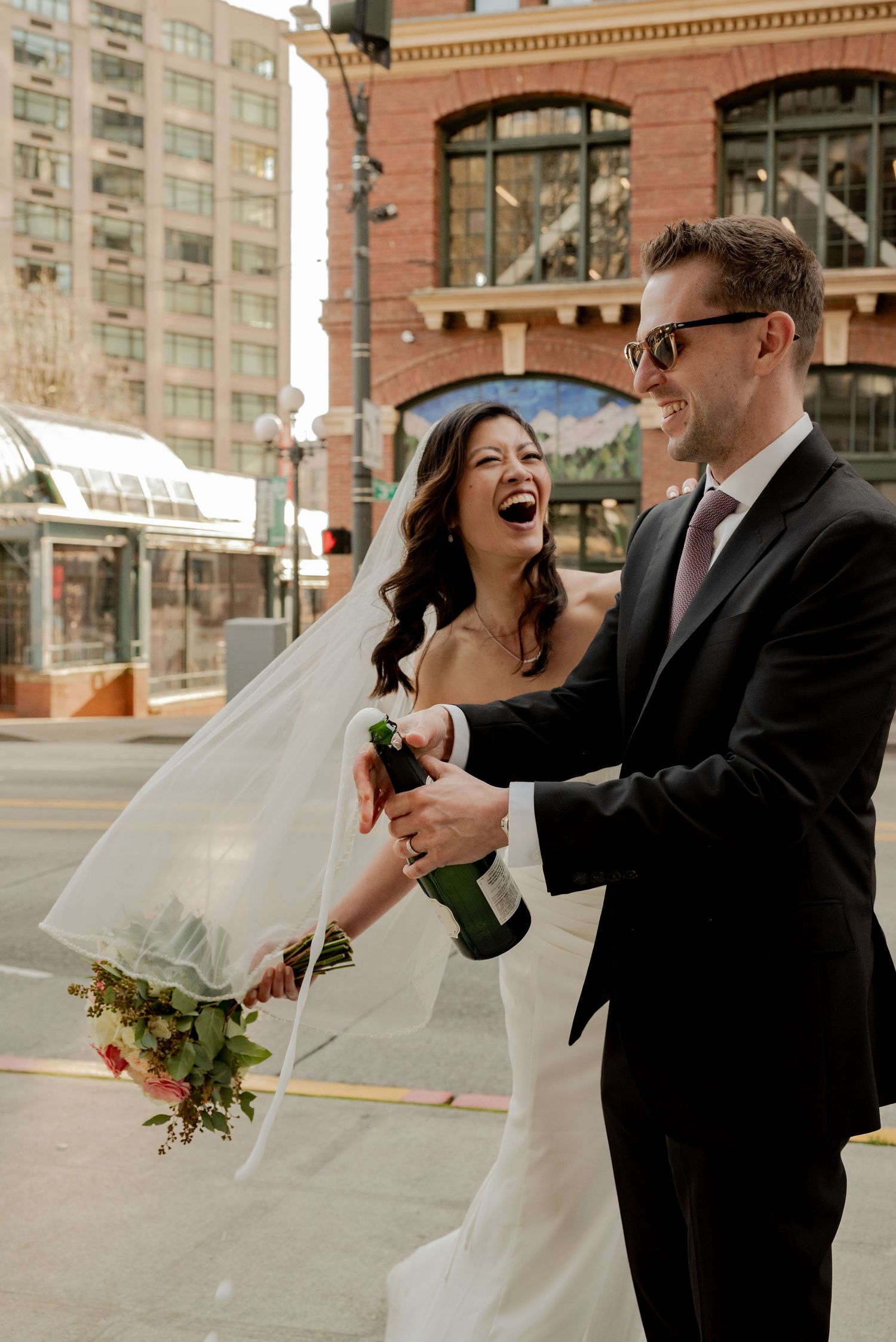Seattle, WA, A couple shares a joyful moment together on their wedding day in an urban setting with brick buildings in the background.