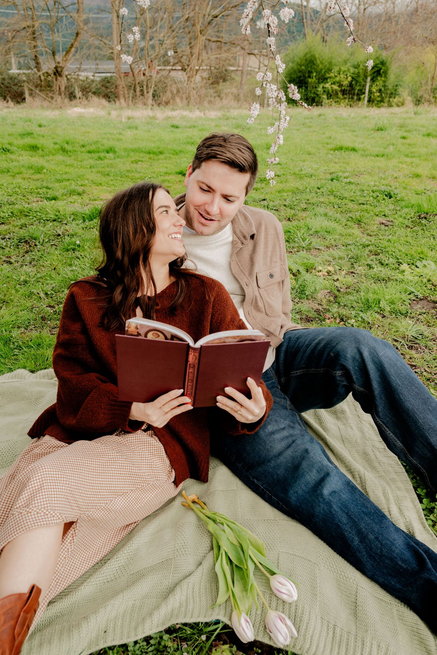 Deming, Washington, A couple shares an intimate moment while reading together on a blanket in a grassy field with tulips beside them.