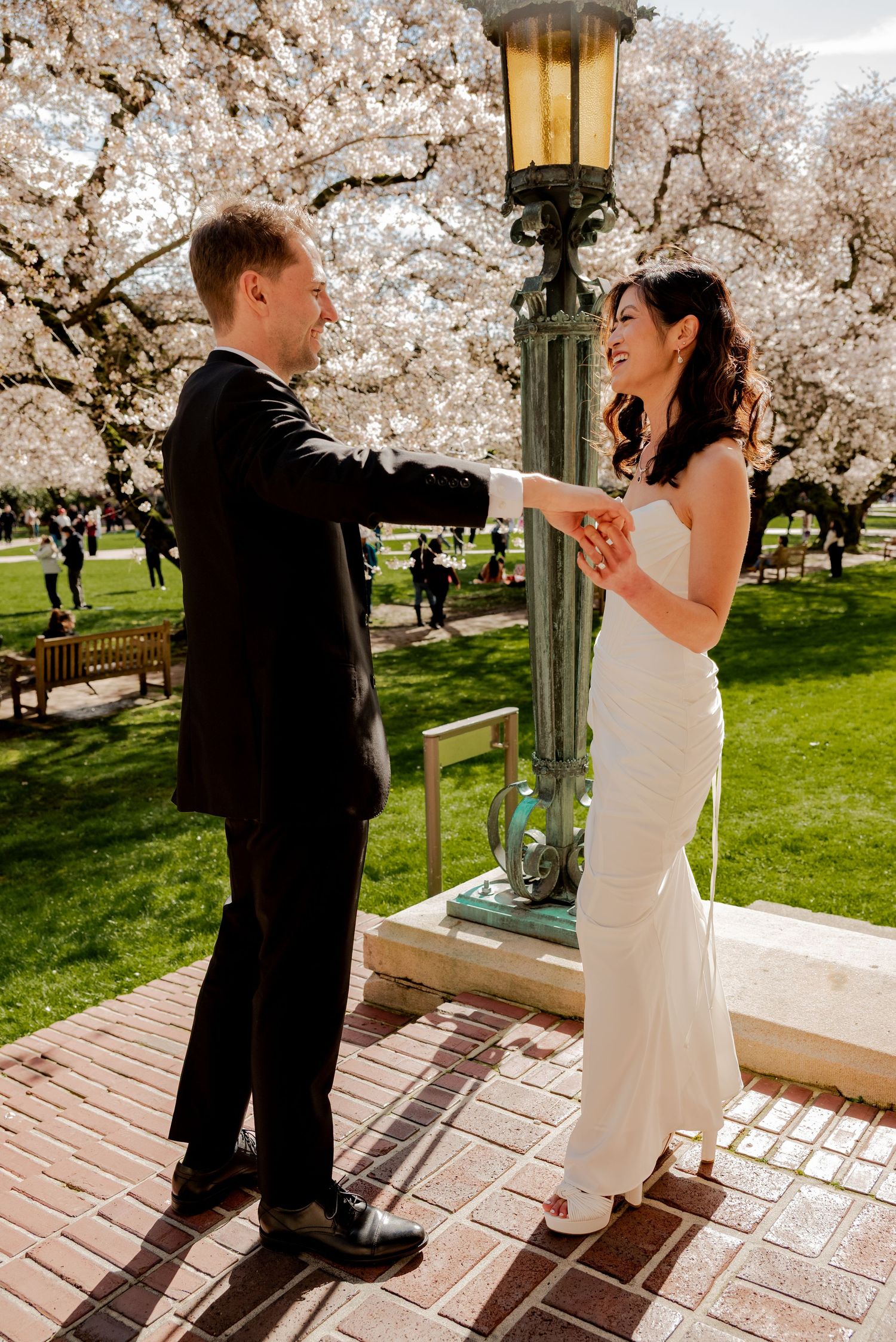 Seattle, Washington, A couple shares a joyful moment under blooming cherry blossoms next to a vintage lamppost on a brick patio.
