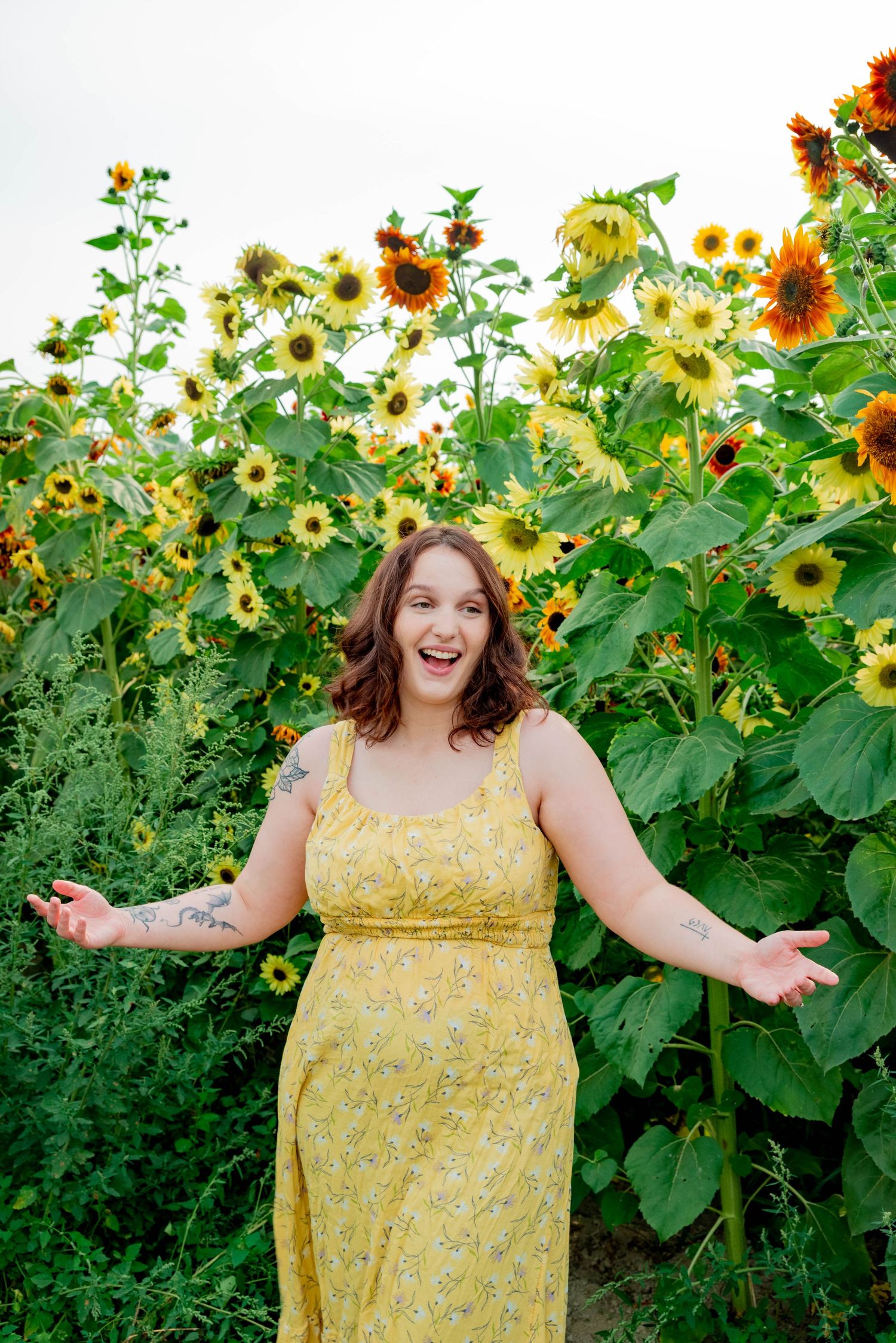 A cheerful figure in a yellow floral dress poses joyfully in front of a vibrant sunflower field on a sunny day.