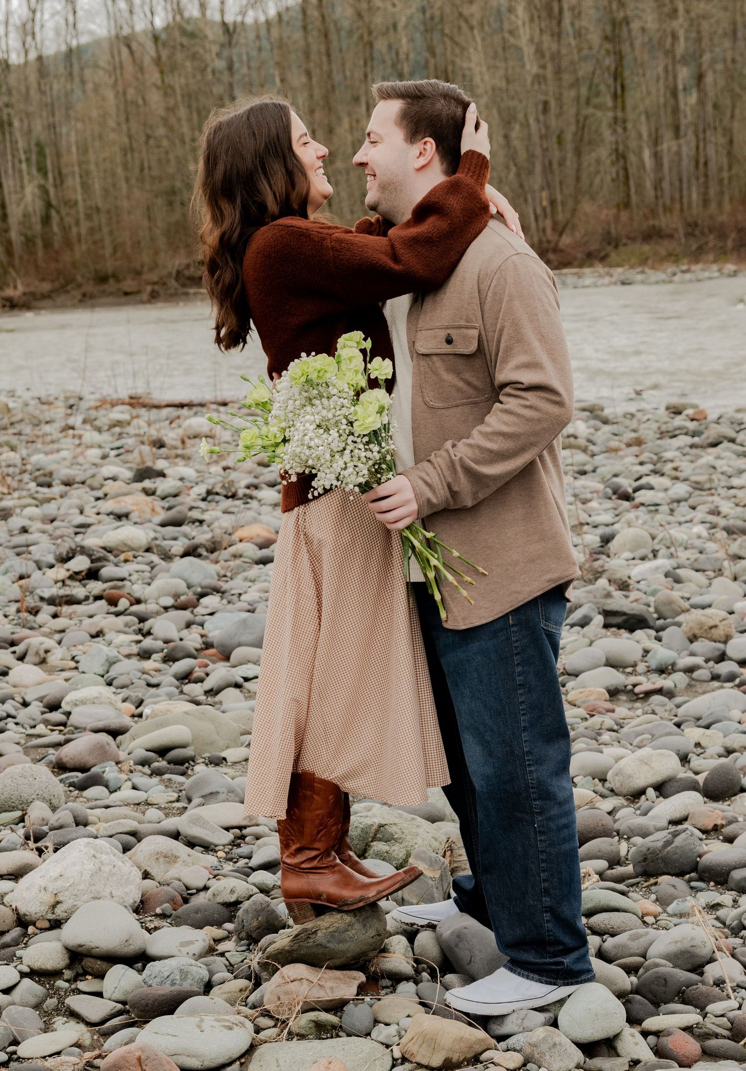 Deming, Washington, A couple shares a romantic moment on the Nooksack River while holding a small bouquet of white flowers in autumn.