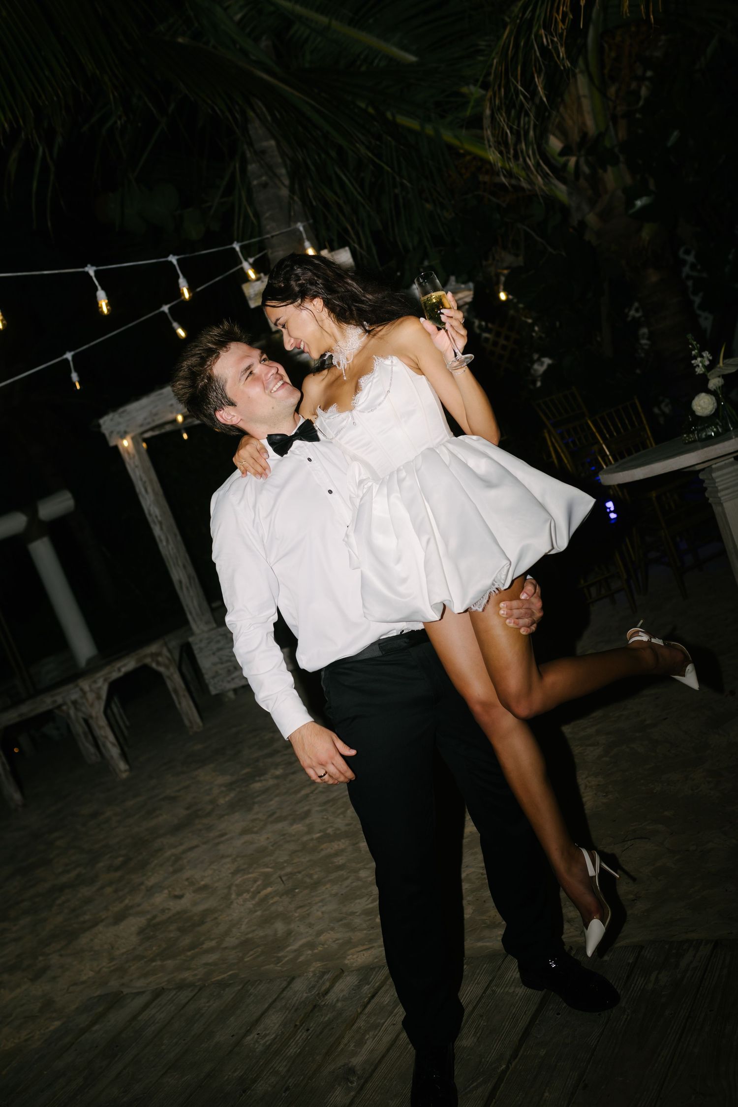 Groom lifting the bride in a short dress during an outdoor evening reception.