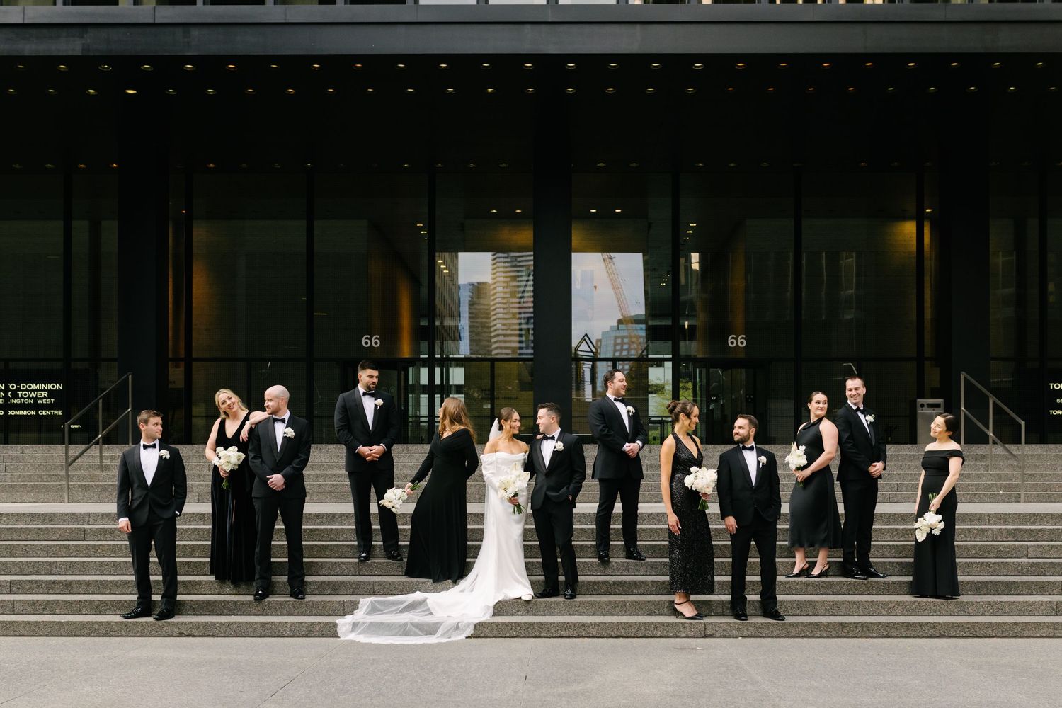Wedding party lined up in front of a downtown Toronto dark modern building facade.