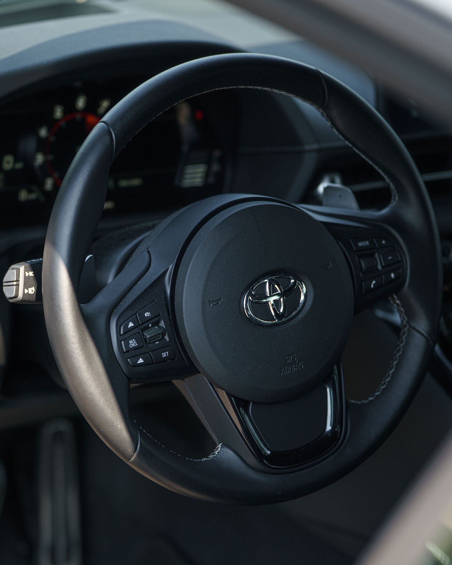 Black leather steering wheel detail of a Toyota car showing various control buttons.