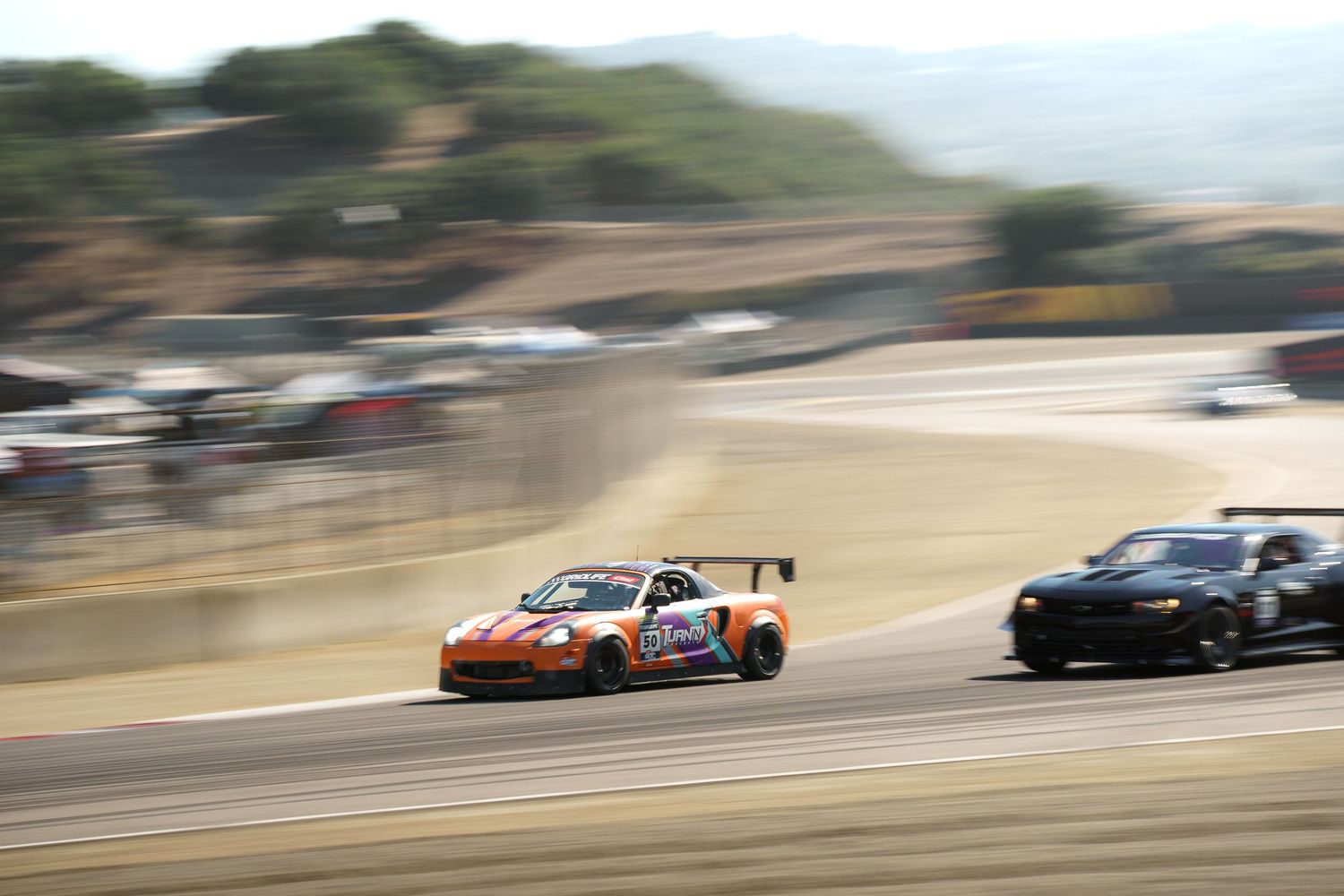 Race cars compete on a winding track during a professional motorsport event at a scenic mountain circuit.