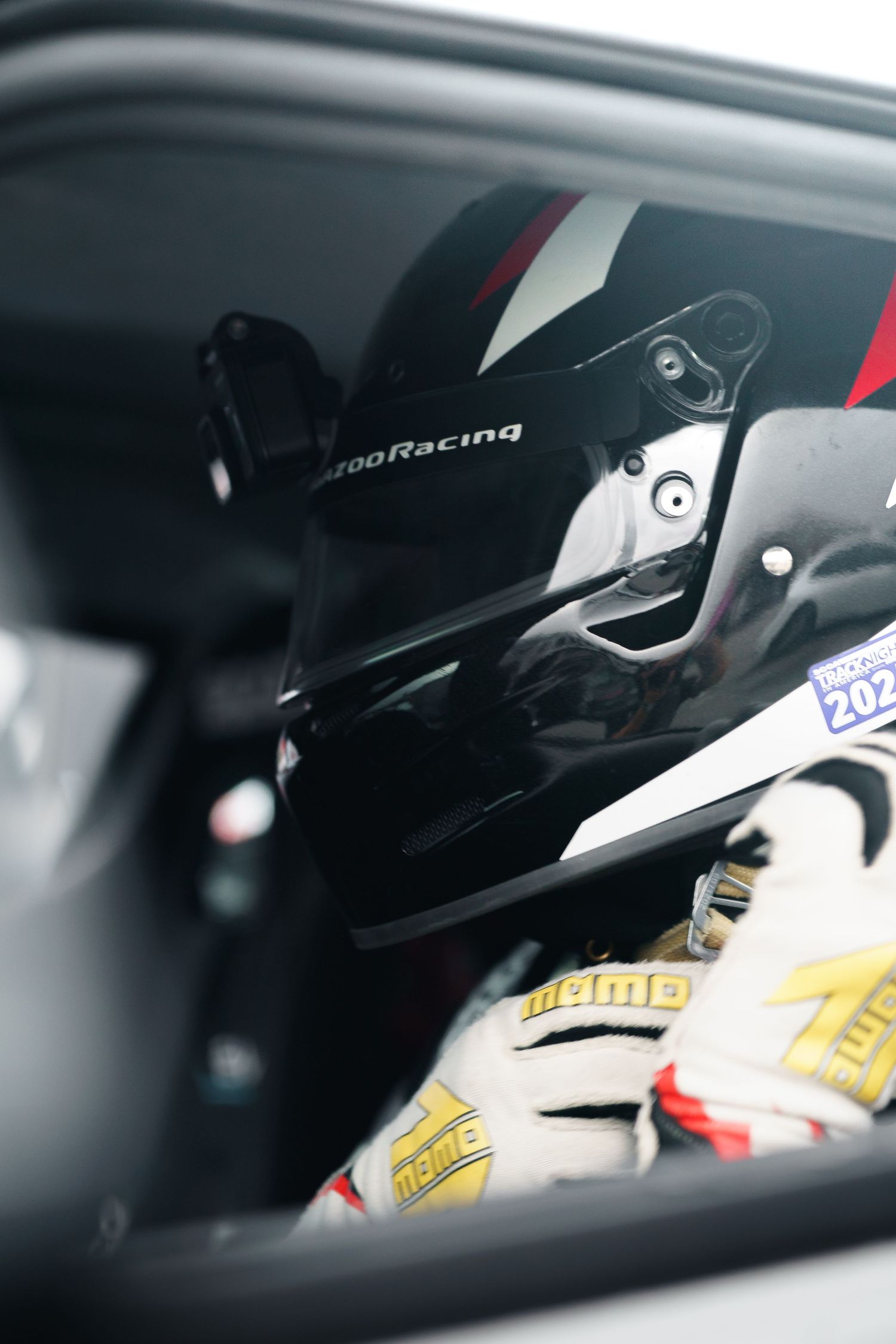 Close-up view of a race car driver wearing a black helmet inside the cockpit during a motorsport event.