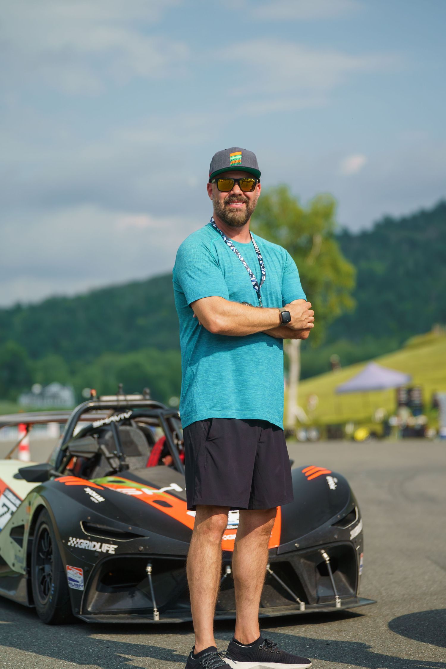 RC race cars parked on asphalt with driver in turquoise shirt and black shorts at remote racetrack.