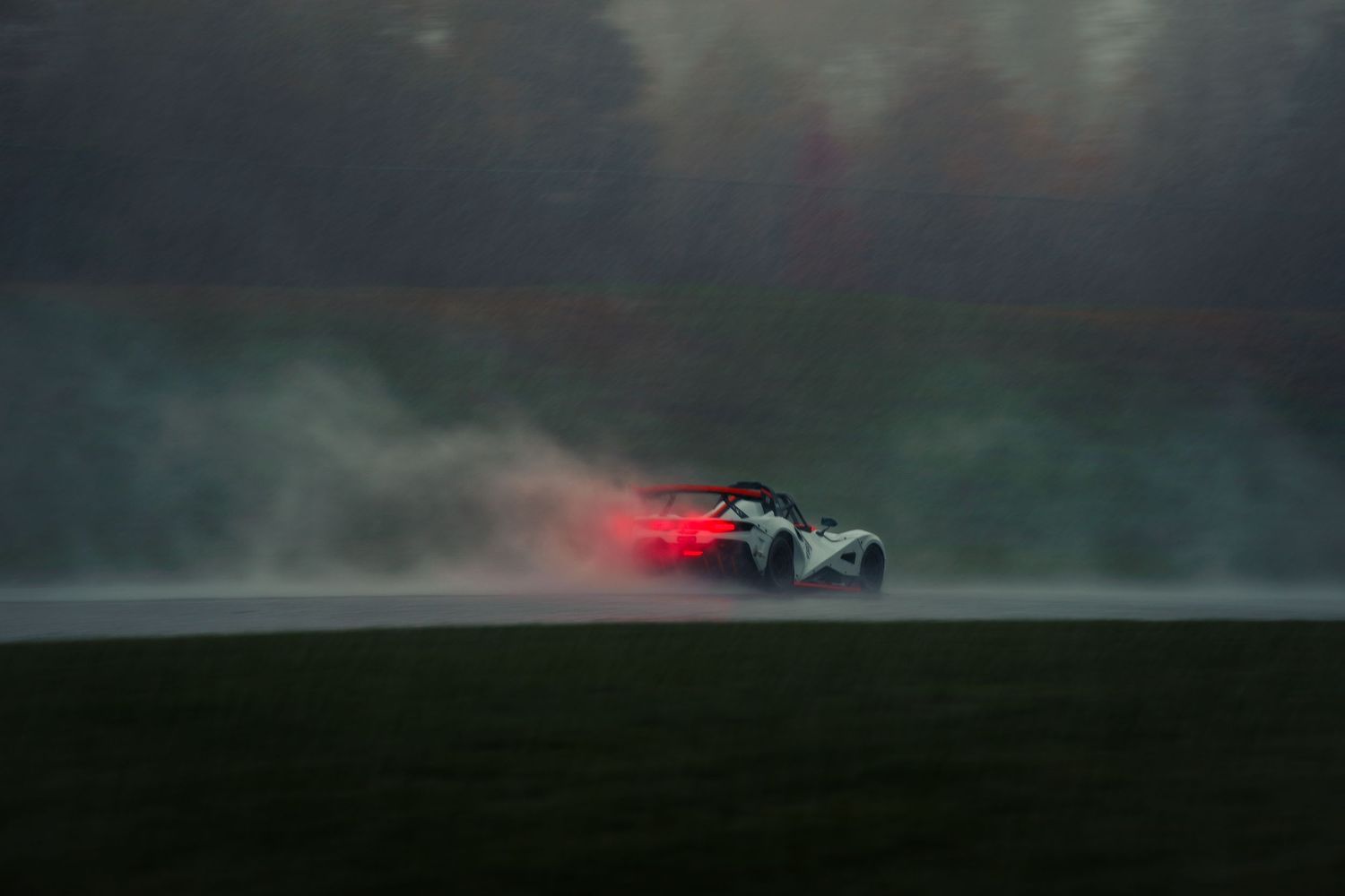 A race car speeds through a misty forest track with glowing red taillights visible in the atmospheric conditions.