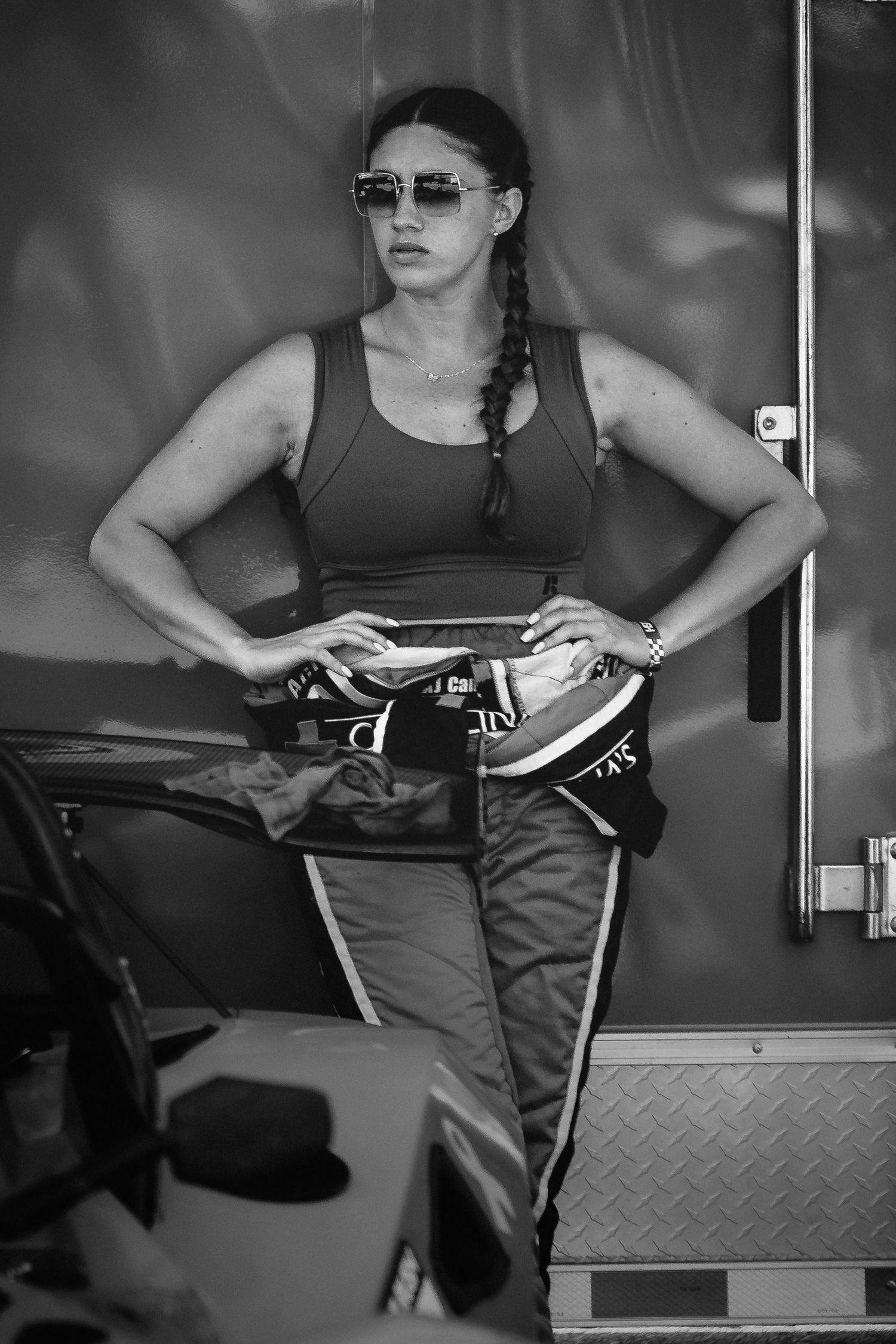 Black and white photo of a fitness enthusiast in sunglasses and athletic wear posing confidently next to exercise equipment.