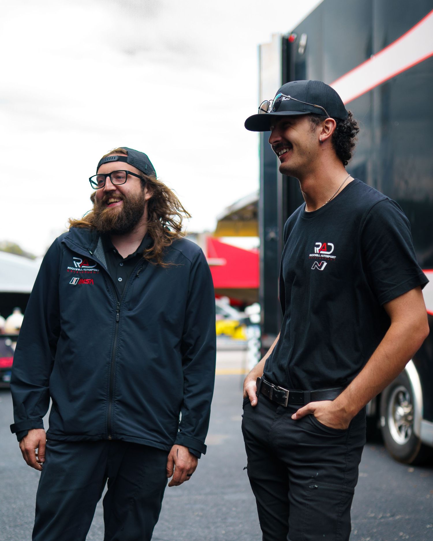 A group of staff members in black uniforms stand together outside in a casual conversation at a workplace.