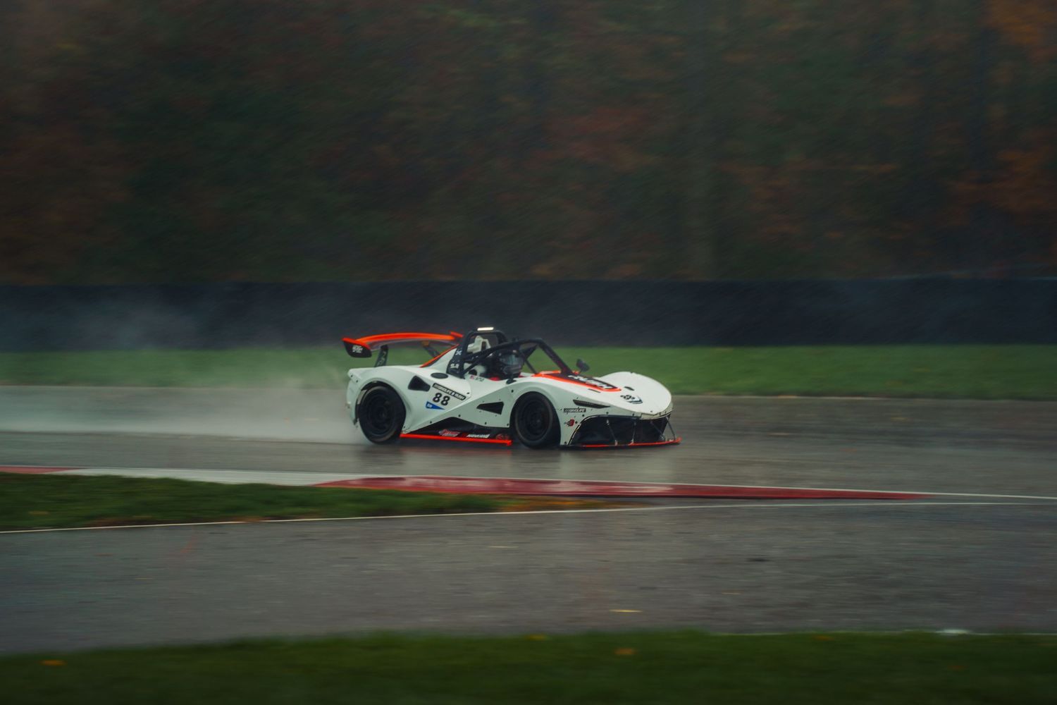 Formula E racing car speeds through a wet racetrack with spray flying during an intense competition.