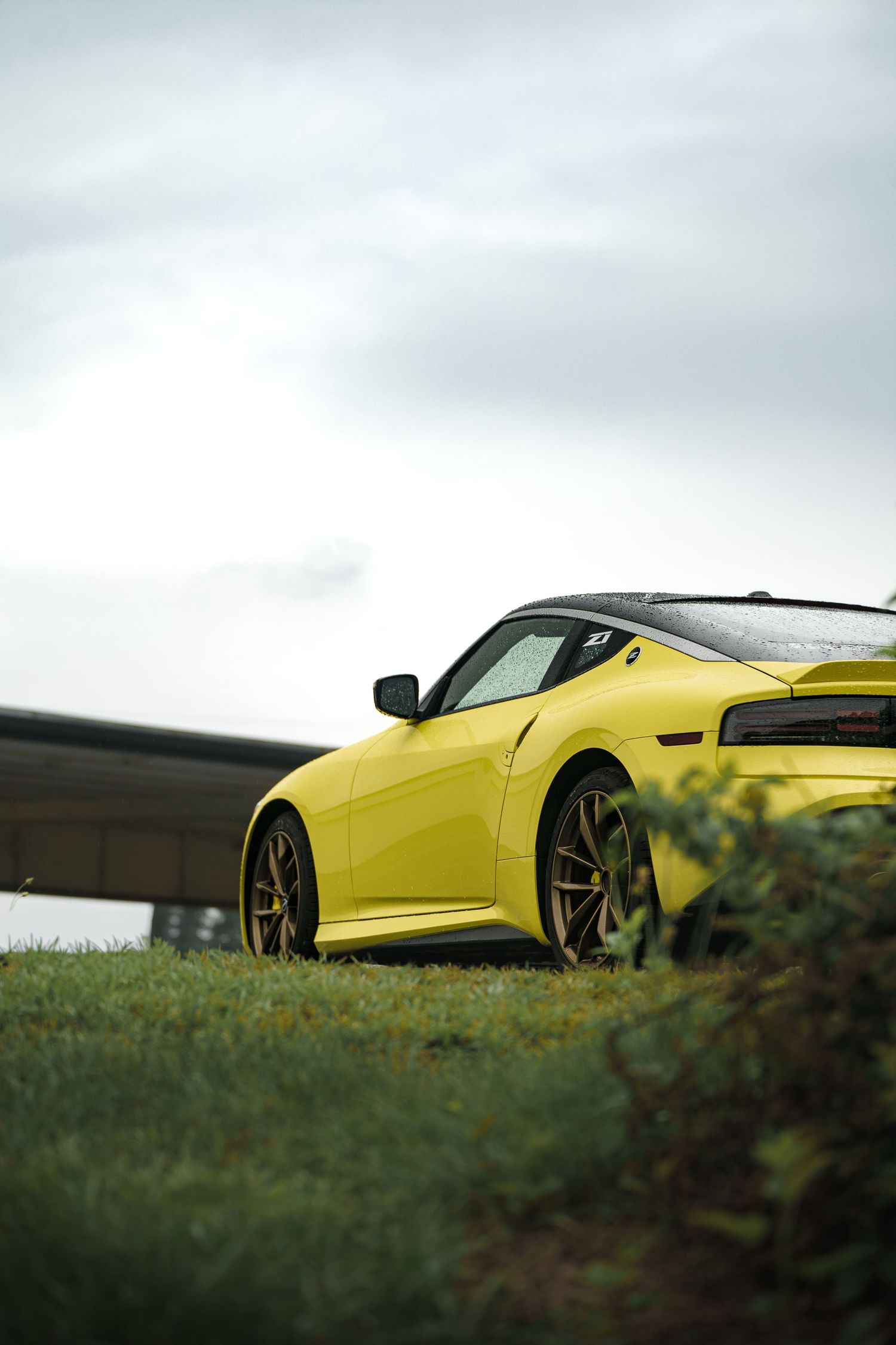 Yellow BMW M4 photographed from a low angle against grass and cloudy sky.