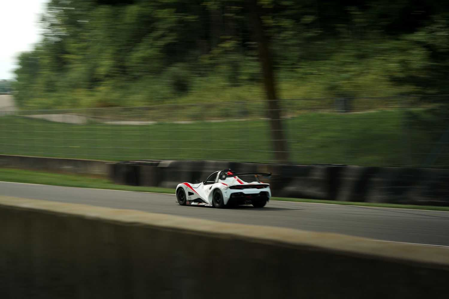 A white sports car races along a winding forest road on a sunny day.