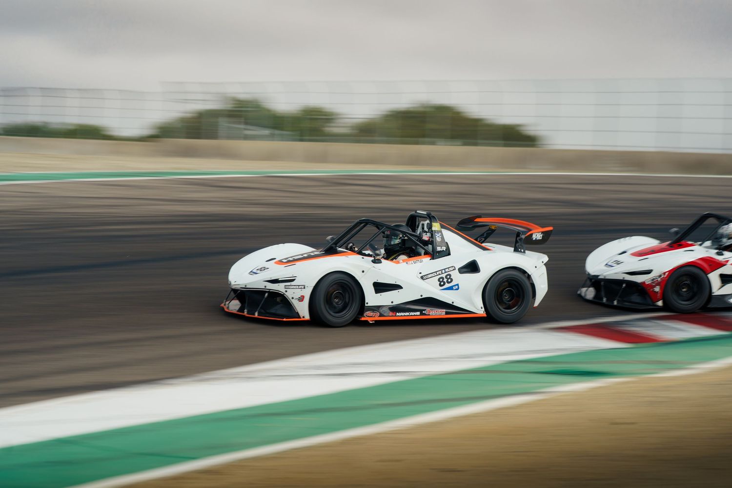 Formula racing cars speed around a track during a competitive motorsport race on a sunny day.