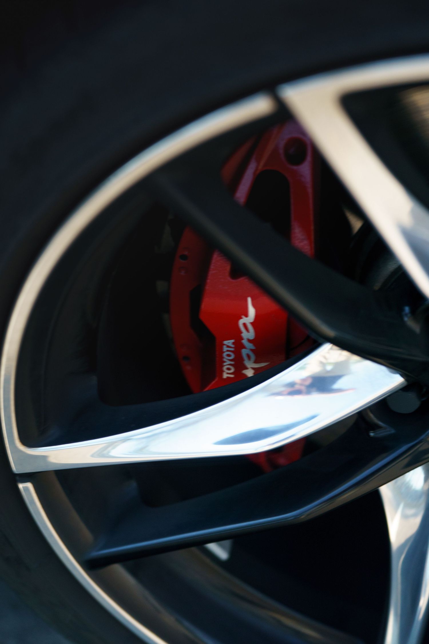 Close-up view of a modern sports car's black and red brake caliper visible through the wheel spokes.