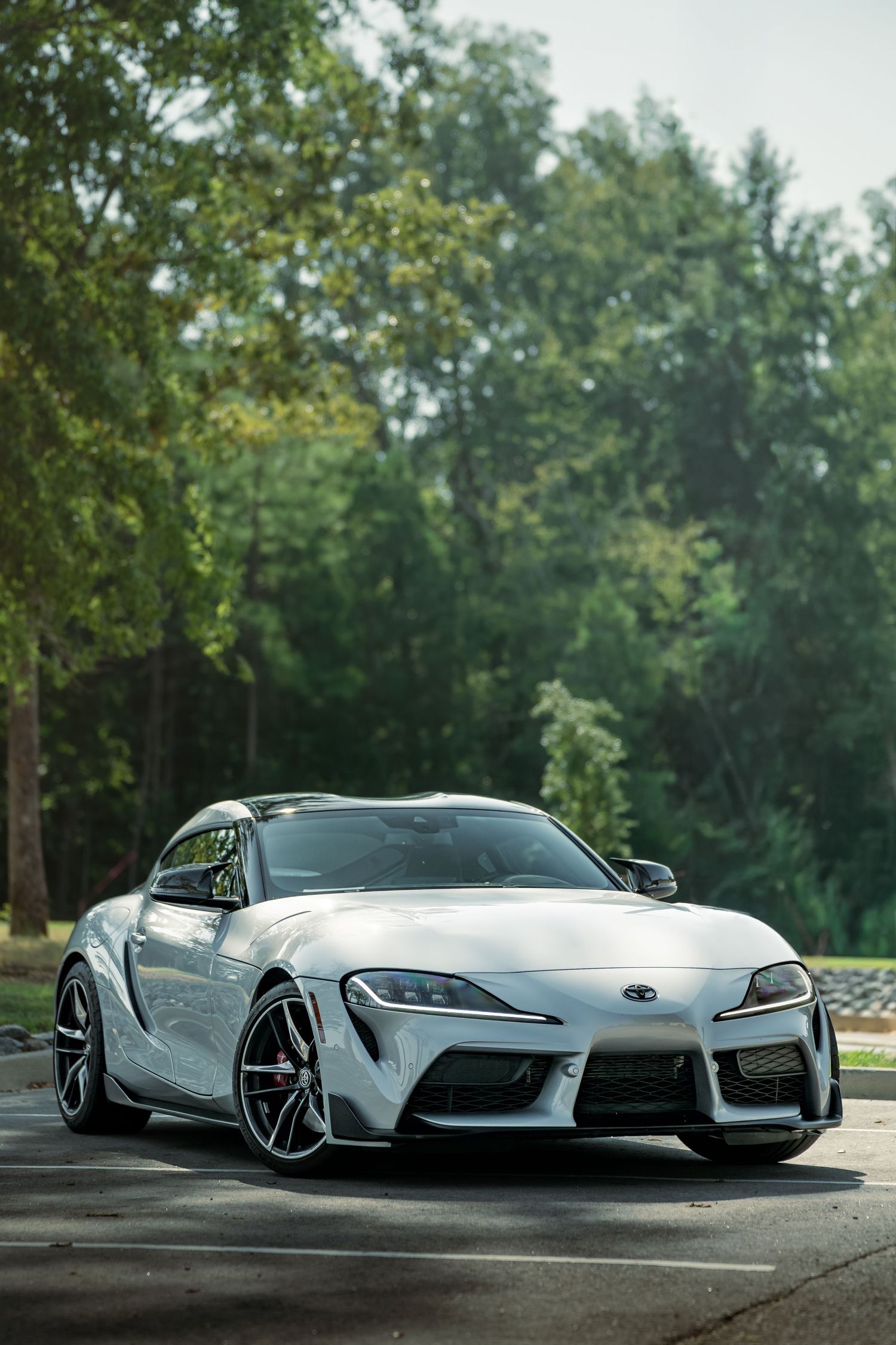 A sleek silver Toyota Supra sports car shown from multiple angles on a curving road with trees in the background.