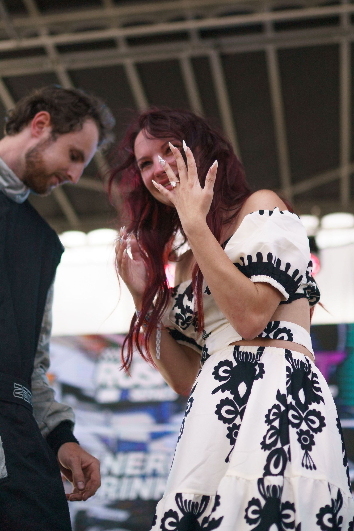 A woman in a black and white patterned dress laughs while gesturing with her hand during an outdoor event.