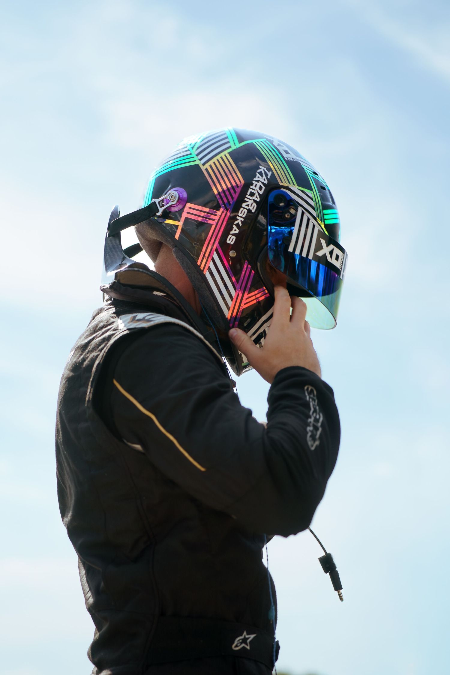 Sequence showing someone putting on a black helmet with colorful geometric patterns against a bright blue sky.