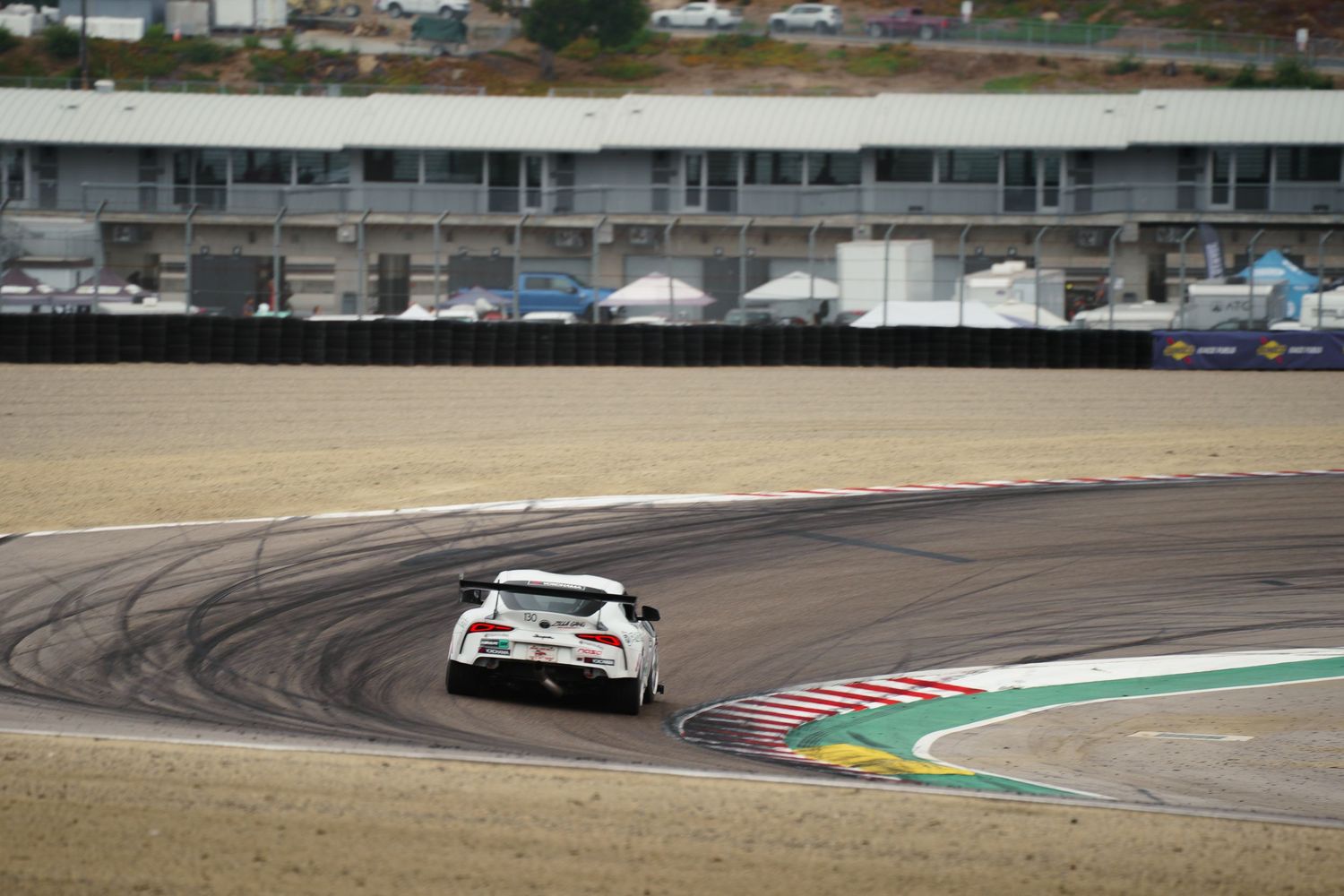 Racing cars speed around a curvy racetrack with tire marks visible on the asphalt surface.