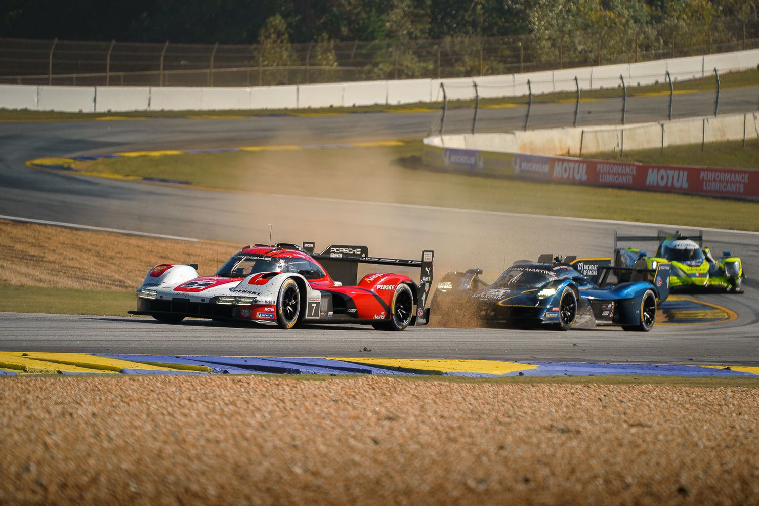 Race cars speed through a winding track during an endurance motorsport competition at sunset.