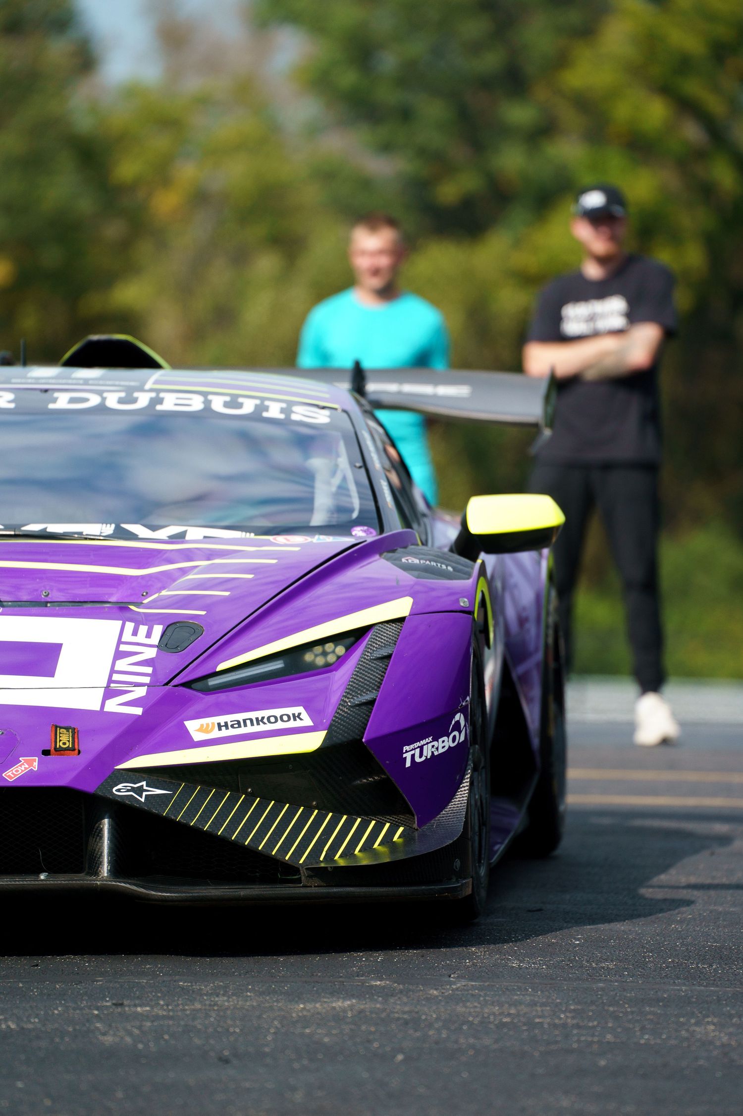 A sleek purple racing car with aerodynamic design and sponsor decals is displayed on an outdoor track.