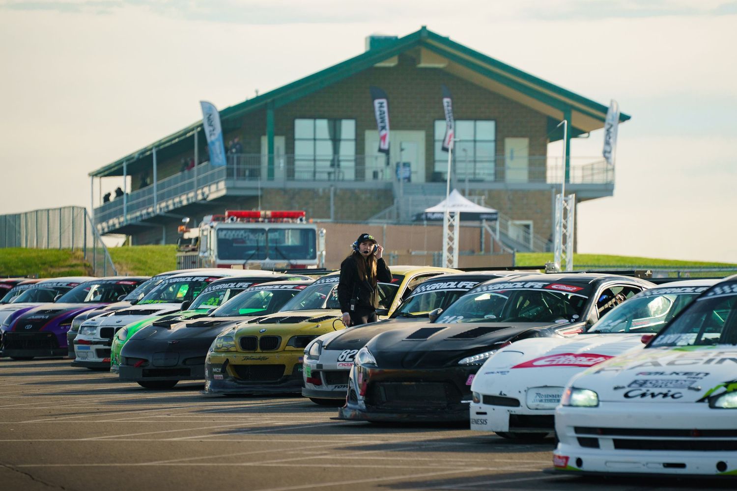 A row of modified sports cars parked in front of a race track building.