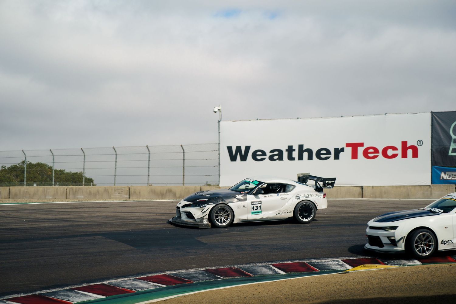 Racing cars line up on a track with WeatherTech branding visible in the background during sunset.