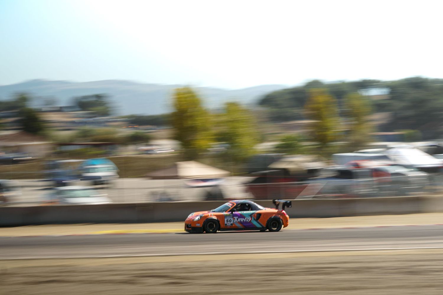 Race cars speed through a curvy track during a competitive motorsport event on a sunny day.