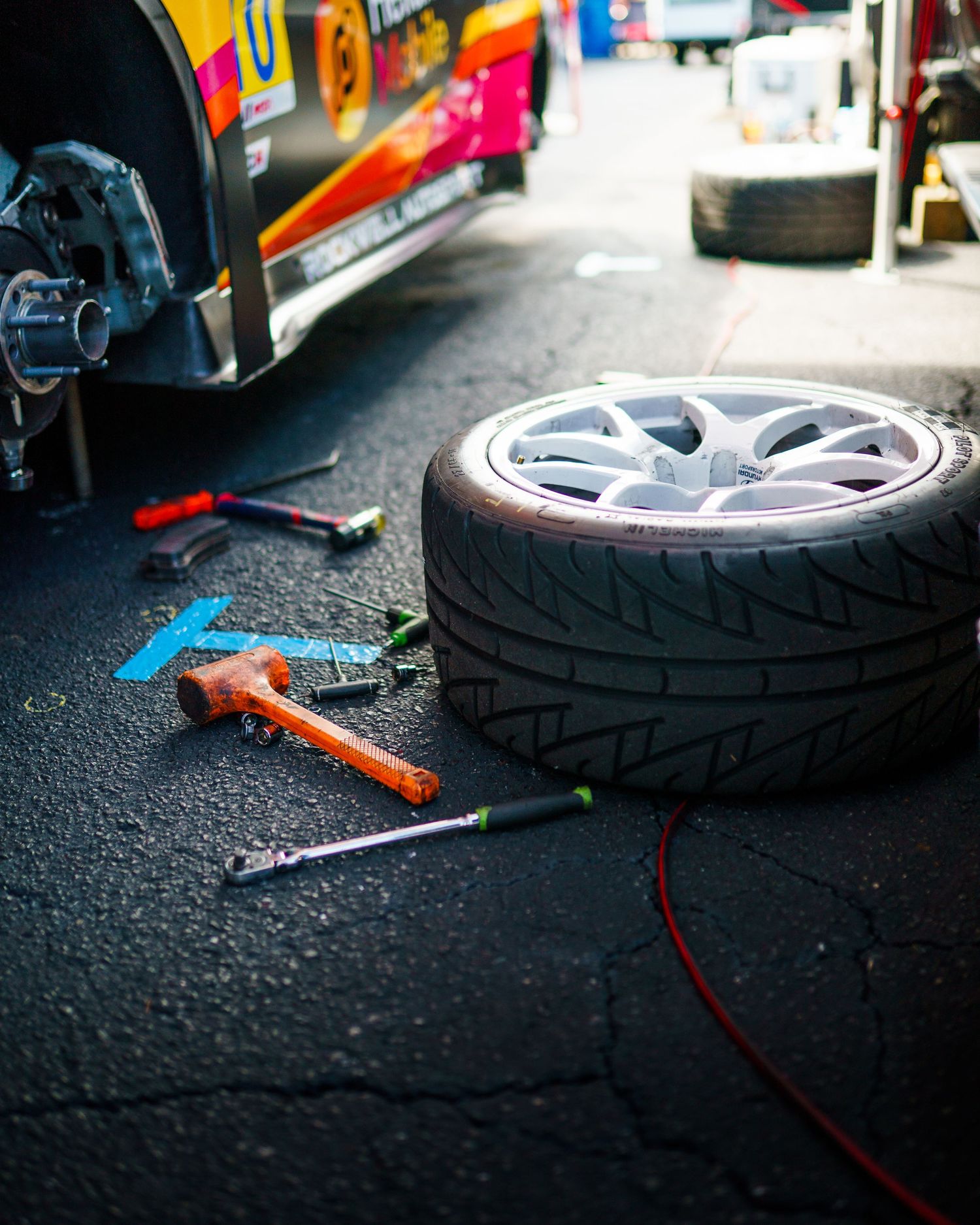Tools and tires laid out on asphalt during a car maintenance session showing repair equipment and wheel parts.