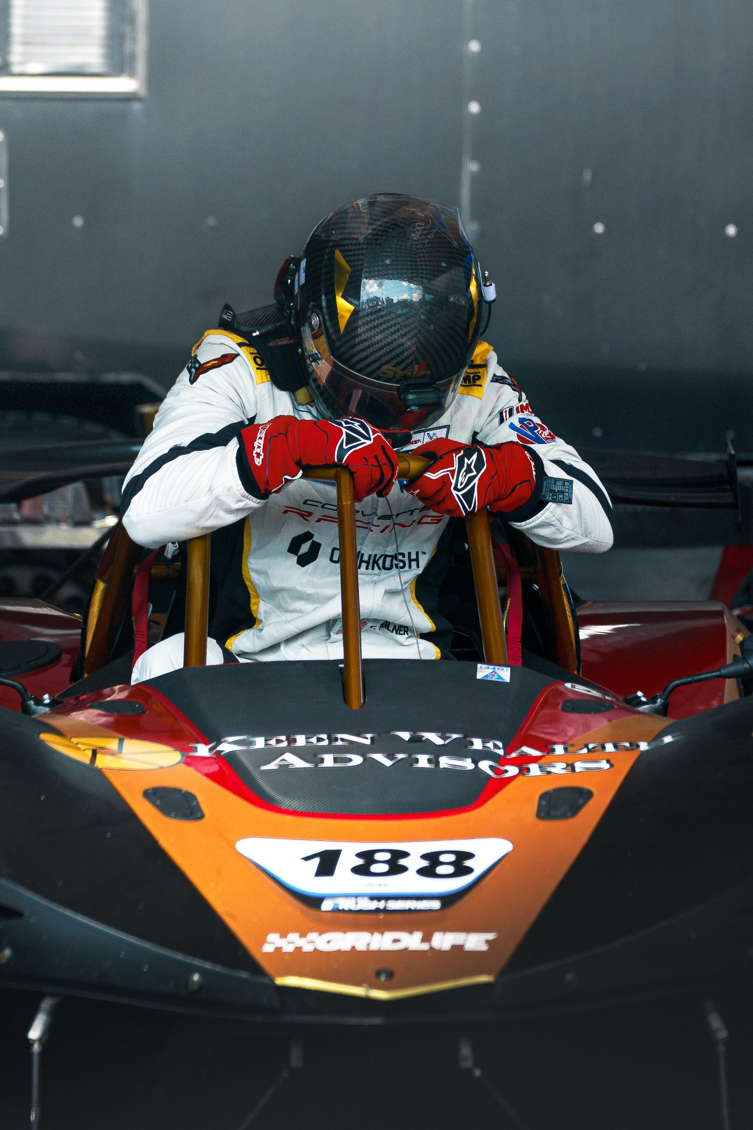 Race driver in protective gear sitting in orange race car cockpit with number 188.