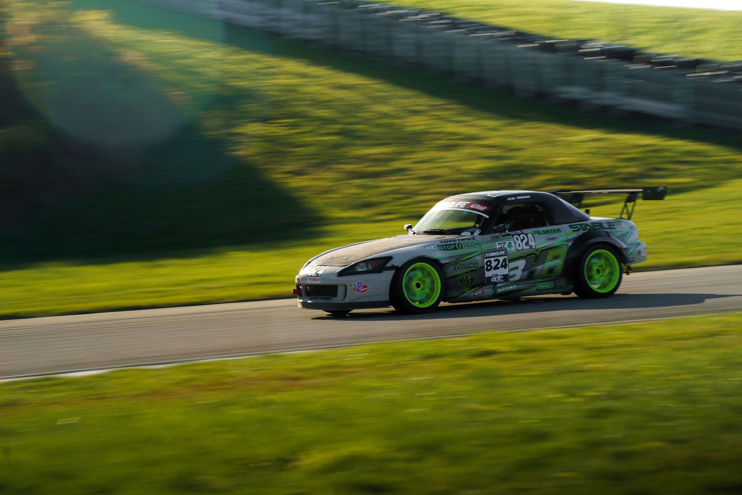 A silver sports car drifts around a green racetrack corner with smoke trailing from its tires.