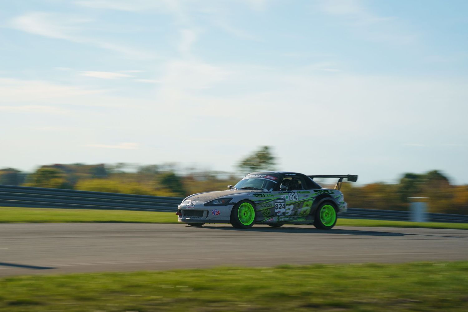 Multiple race cars competing at high speeds on a curvy racetrack with green grass in the background.