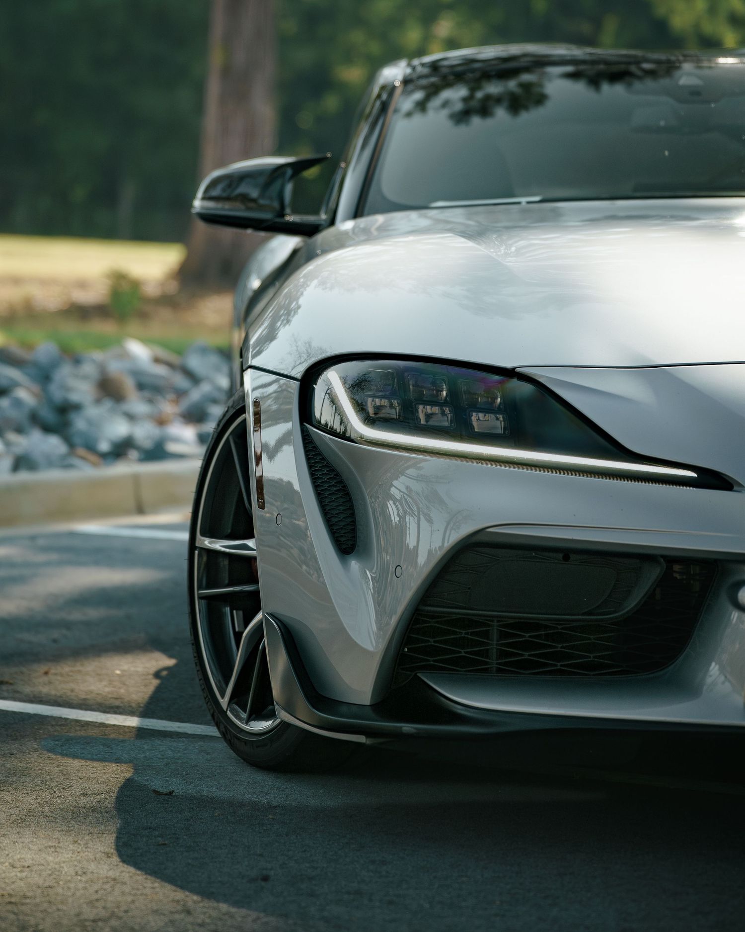 Close-up front bumper detail of a silver Toyota Supra showcasing aggressive styling and air intakes.