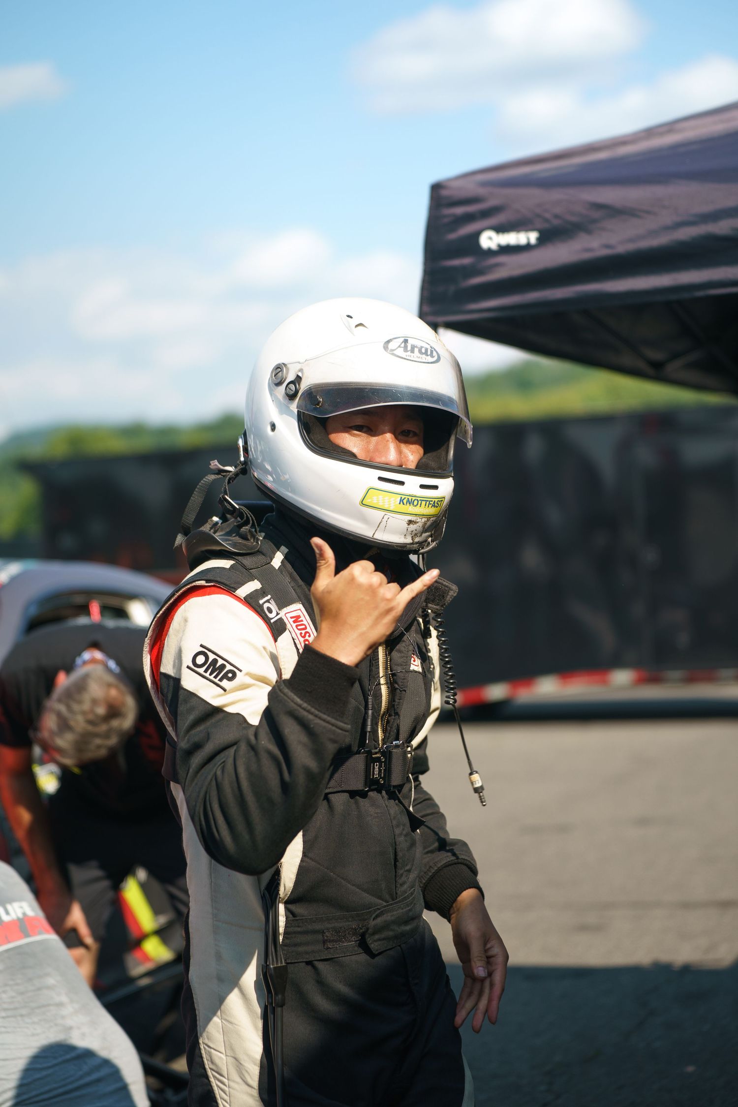 Race car driver in a white helmet adjusting equipment in pit lane at a motorsports track.
