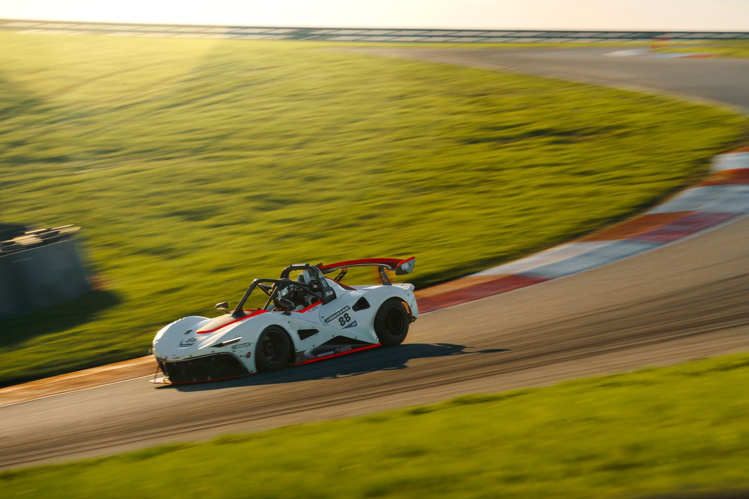 Race cars speed around a winding track during sunset with golden hills in the background.