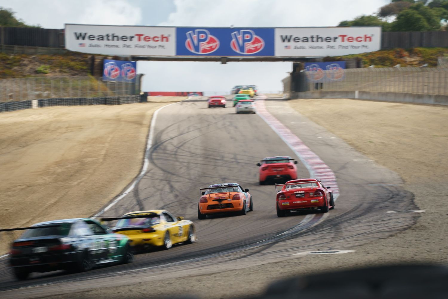 Race cars navigate through a winding track during a competitive motorsport event at WeatherTech Raceway Laguna Seca.