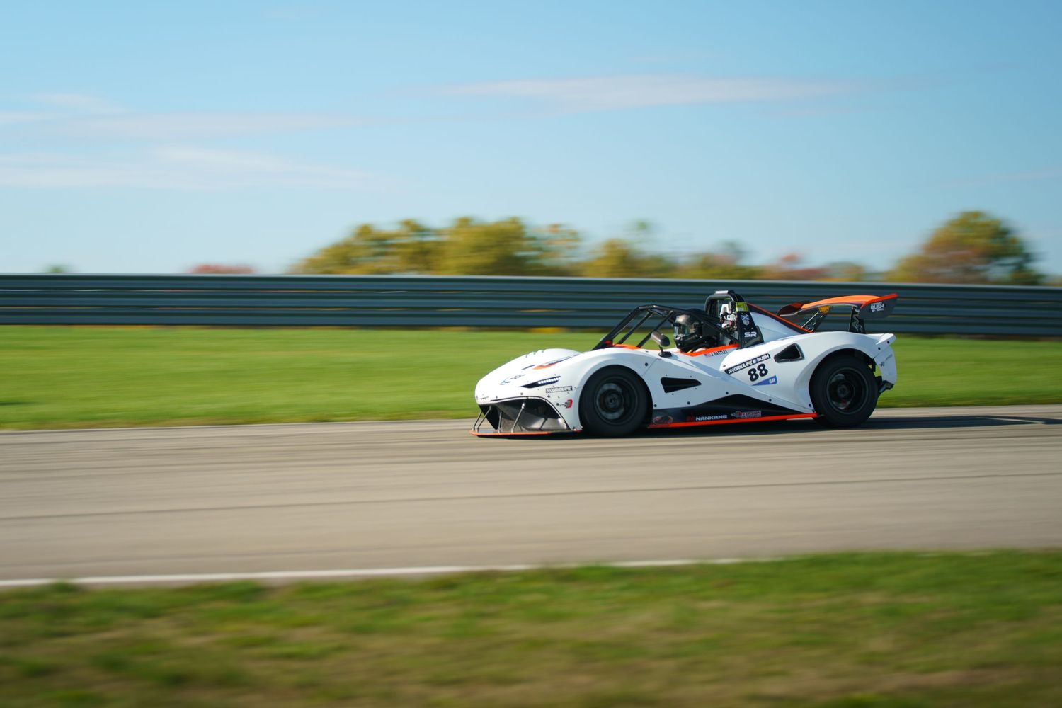 A white race car speeds around a track during a motorsport competition with blurred motion effects.