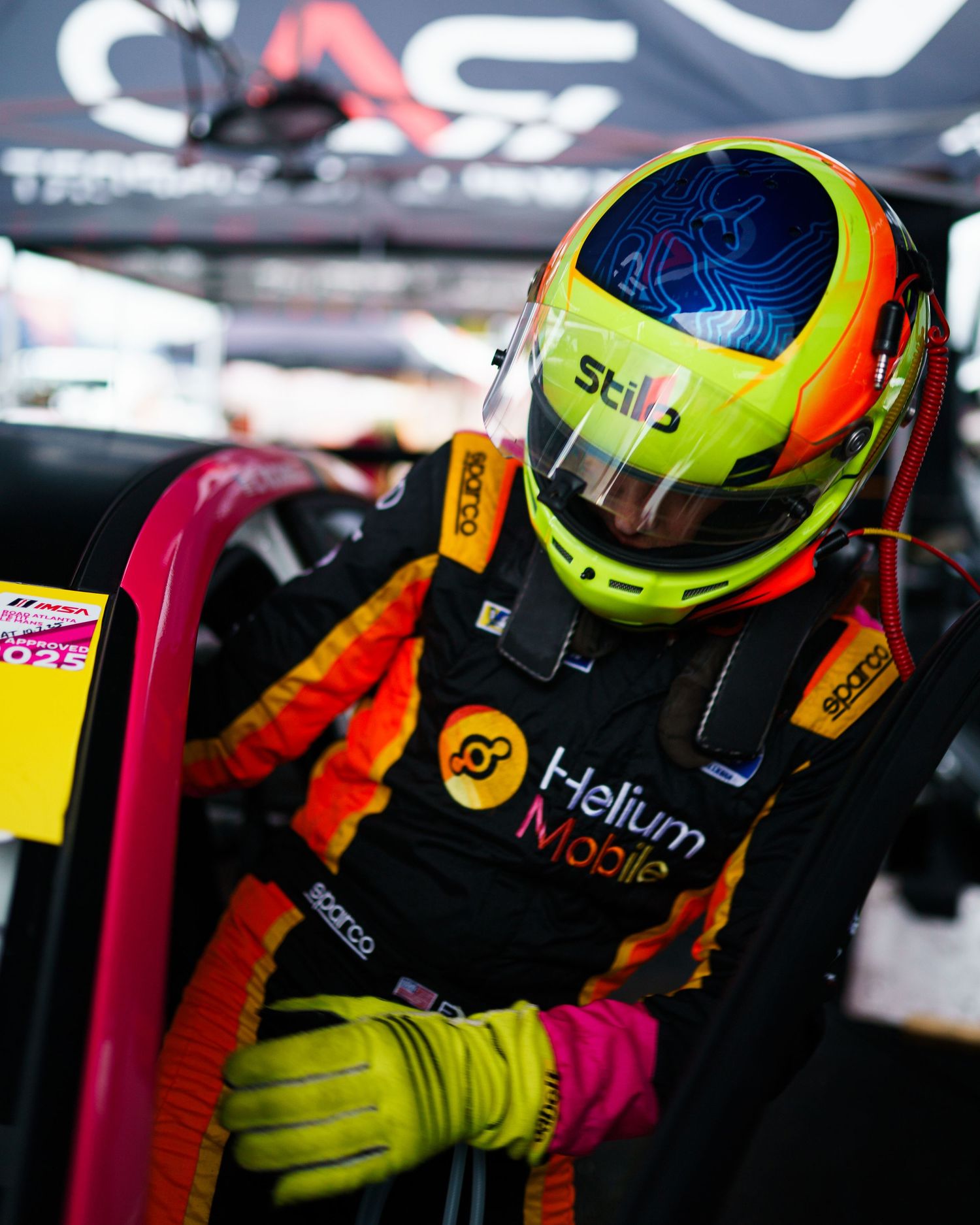 Race car driver in helmet and racing suit sits in cockpit preparing for competition.