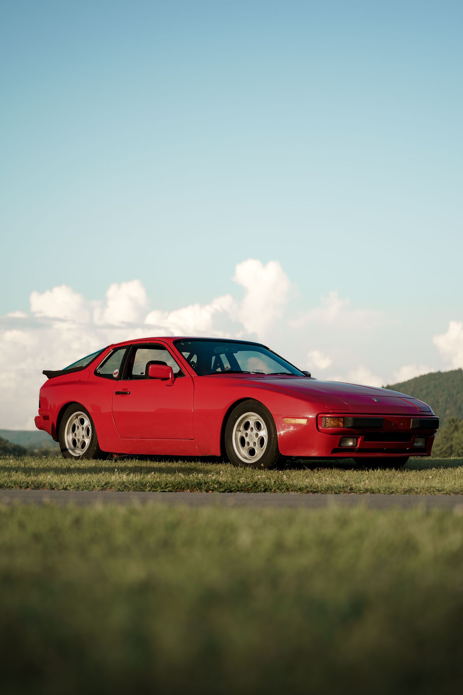Red Porsche 928 photographed from side profile against rolling hills and blue sky.