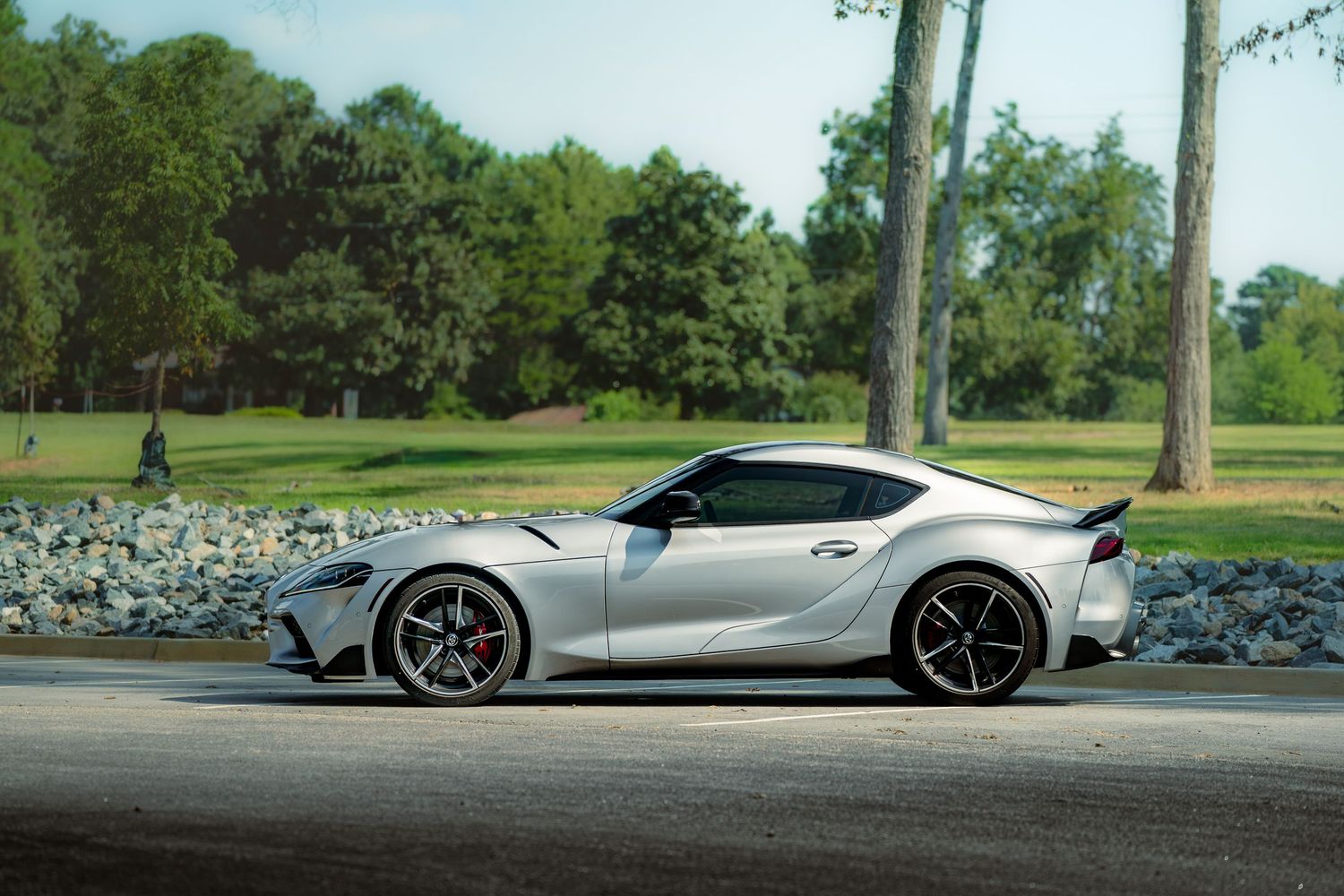 Low-angle view of a silver Toyota Supra showcasing its sleek silhouette against trees and grass.