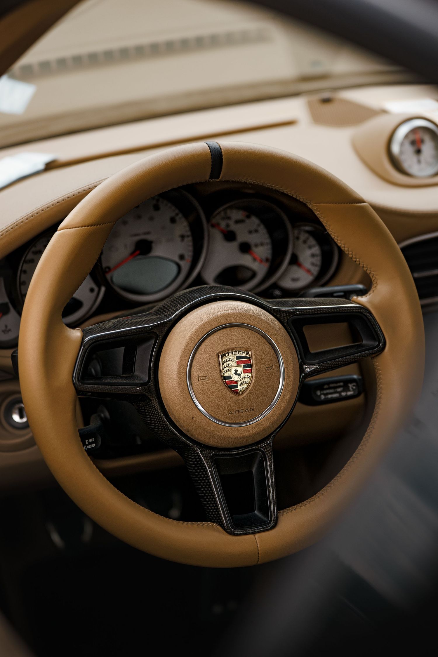 Close-up shots of a Porsche steering wheel and dashboard featuring tan leather interior details.