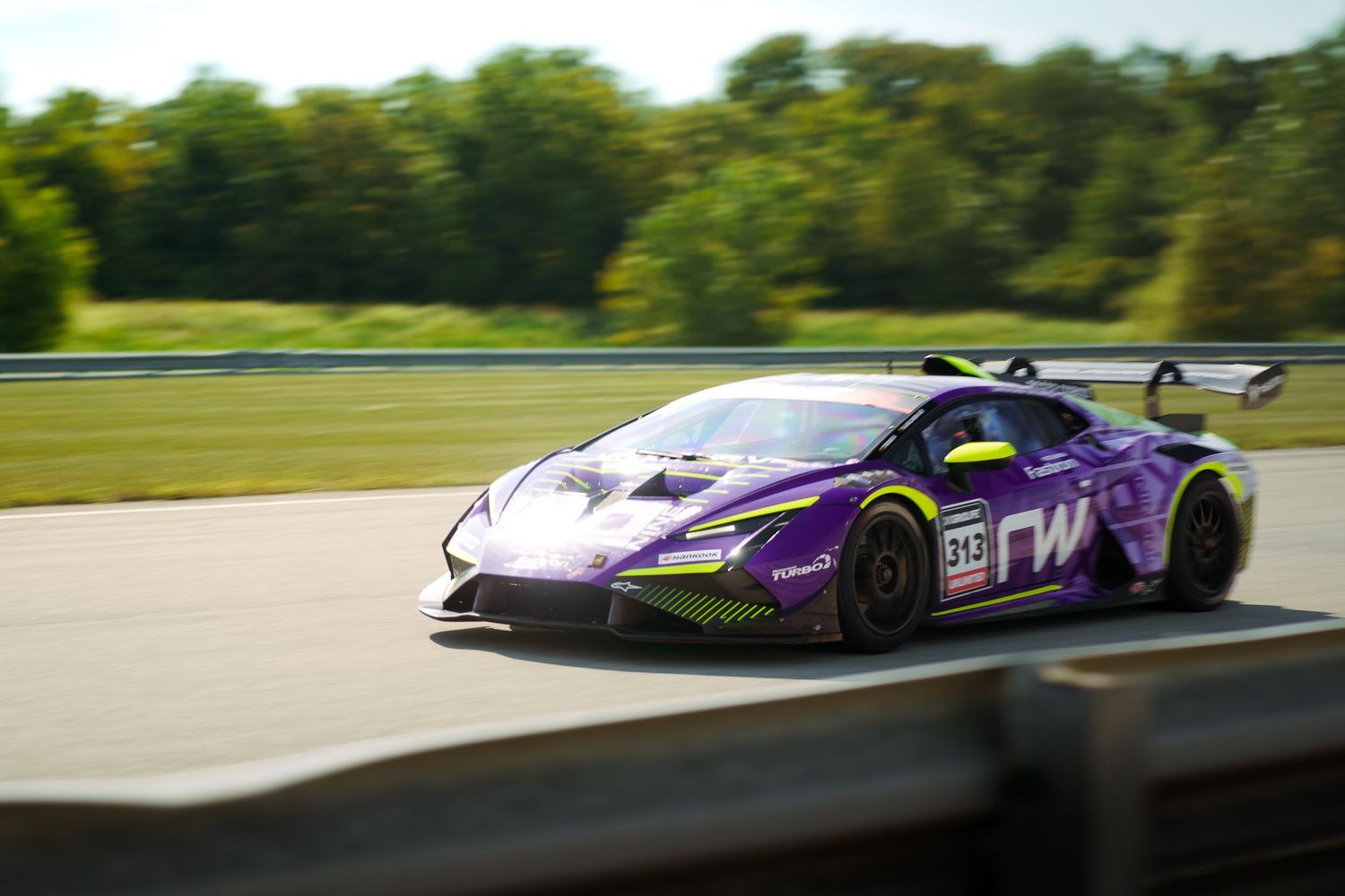 Purple and white racing car speeds around a racetrack during a competitive motorsport event.