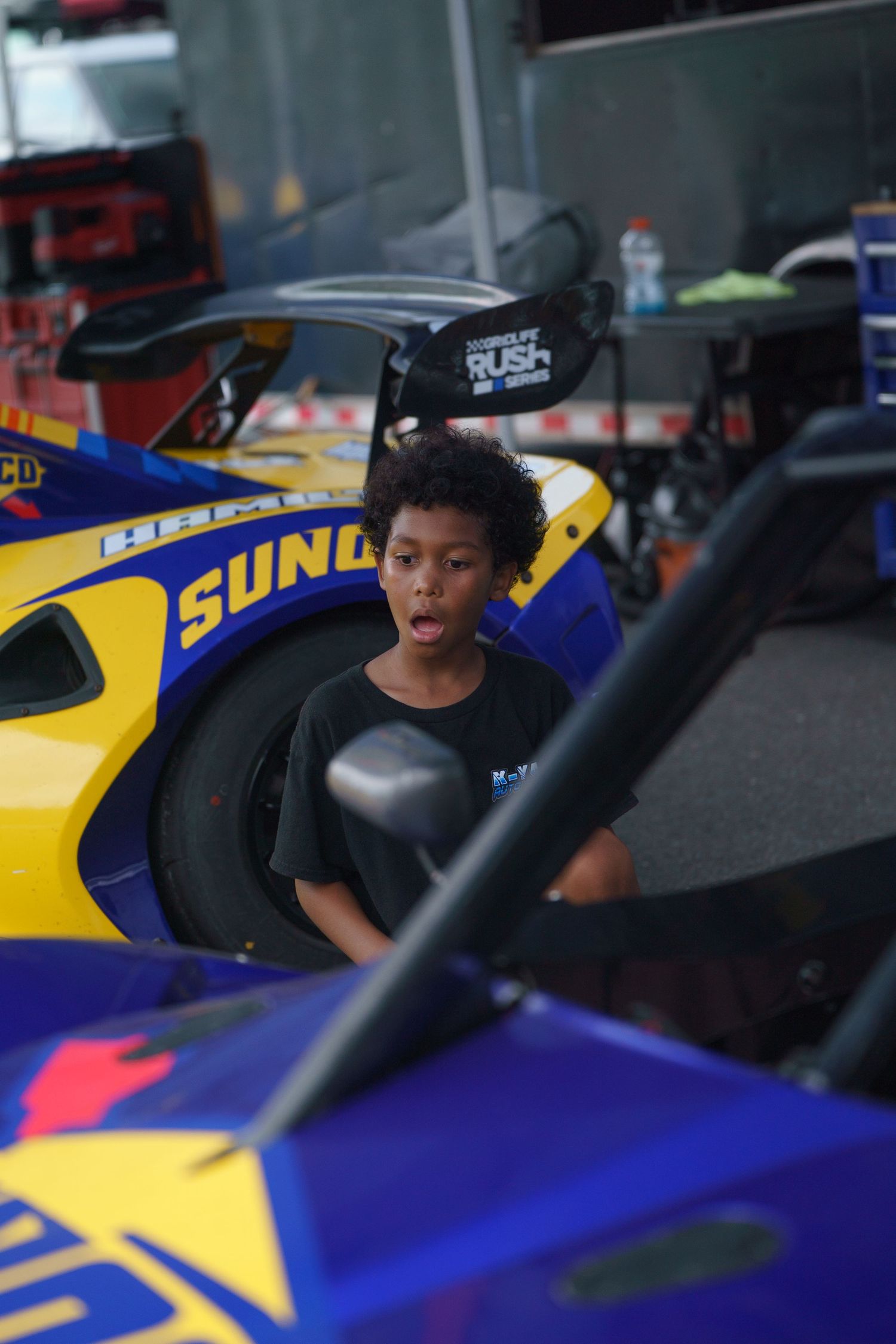 A person sits in a yellow and blue Sunoco racing car at a motorsports event.