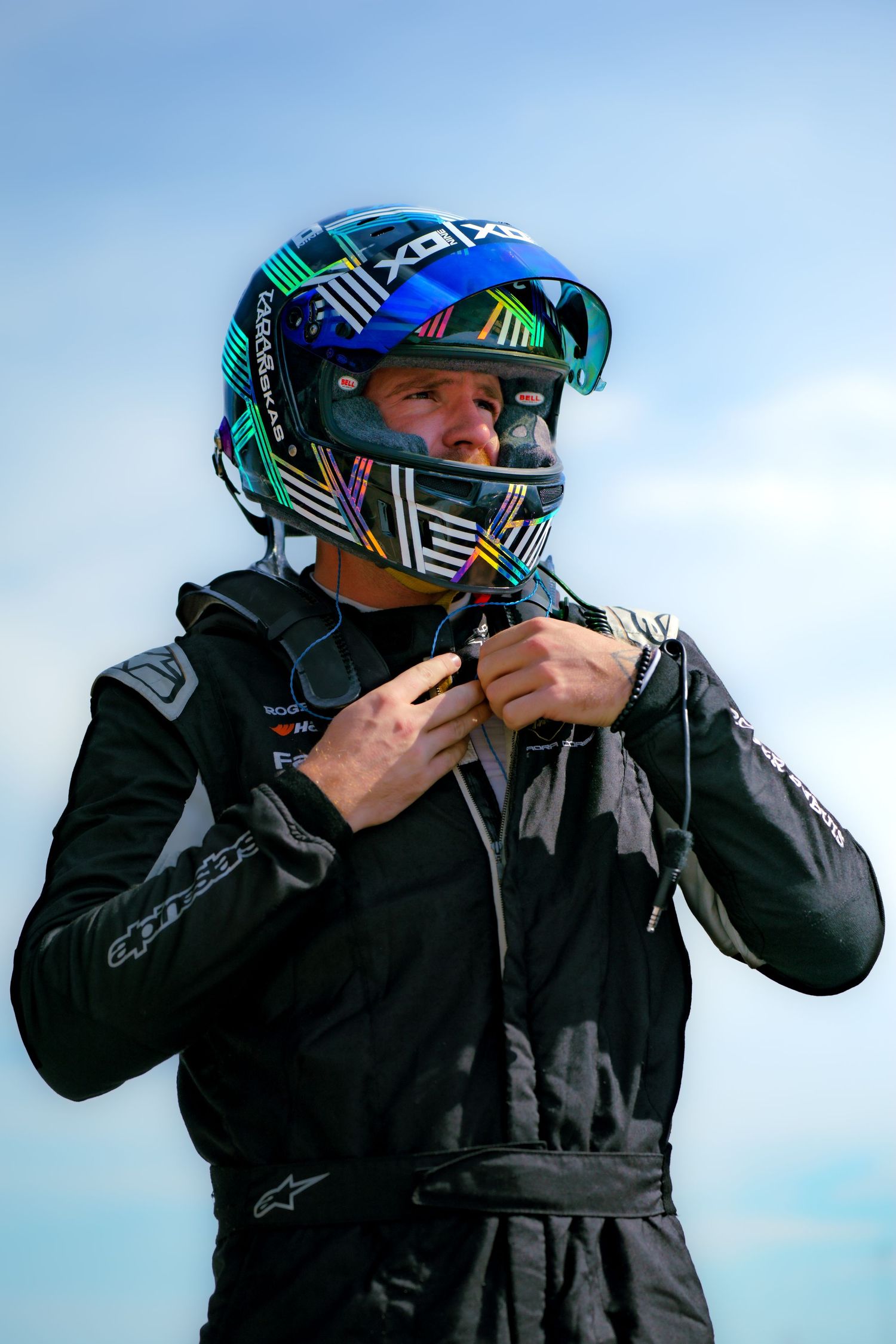 Person adjusting a motocross helmet with vibrant geometric designs and teal visor in outdoor setting.