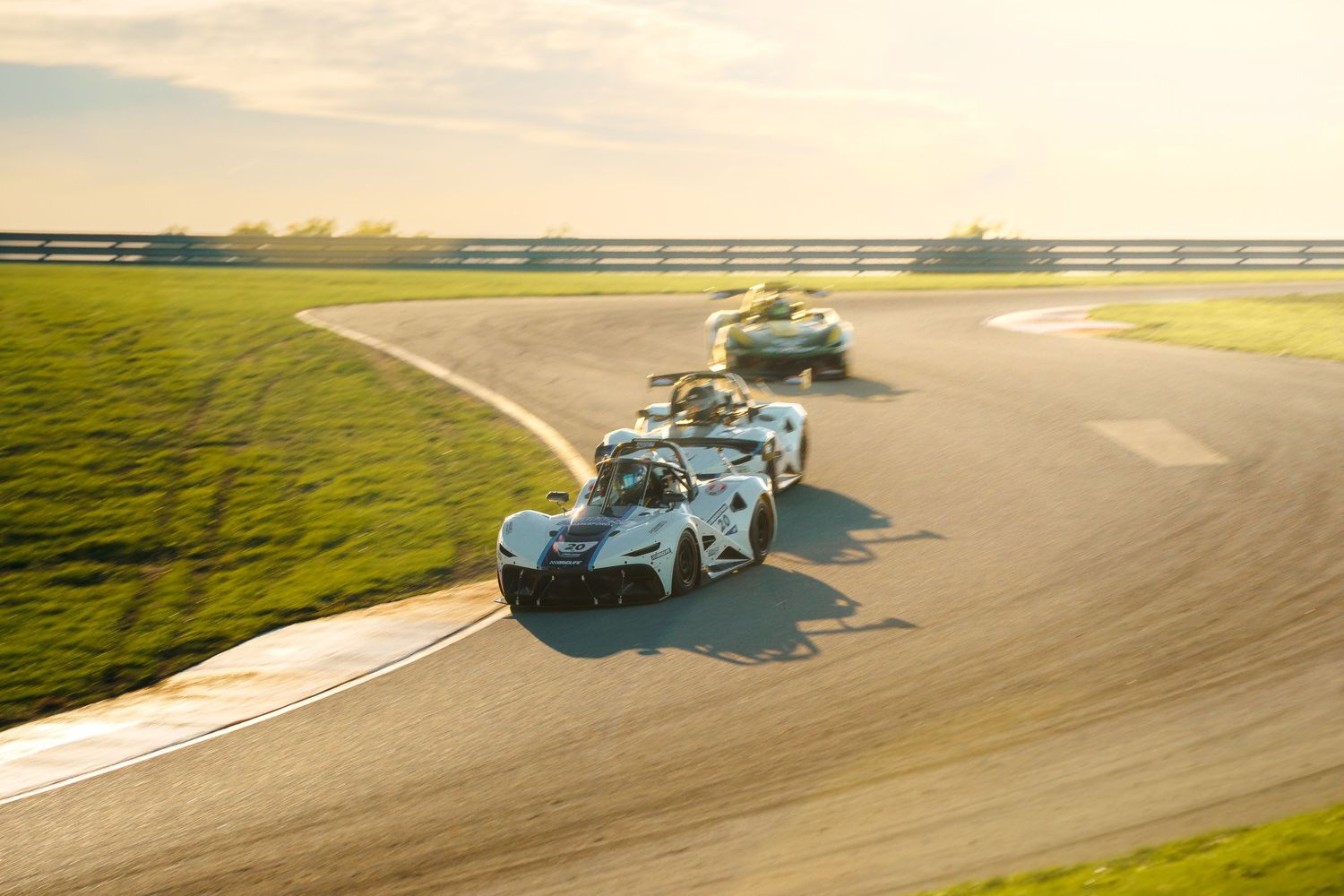 A silver sports car races around a winding racetrack curve during a sunny day at a professional racing circuit.